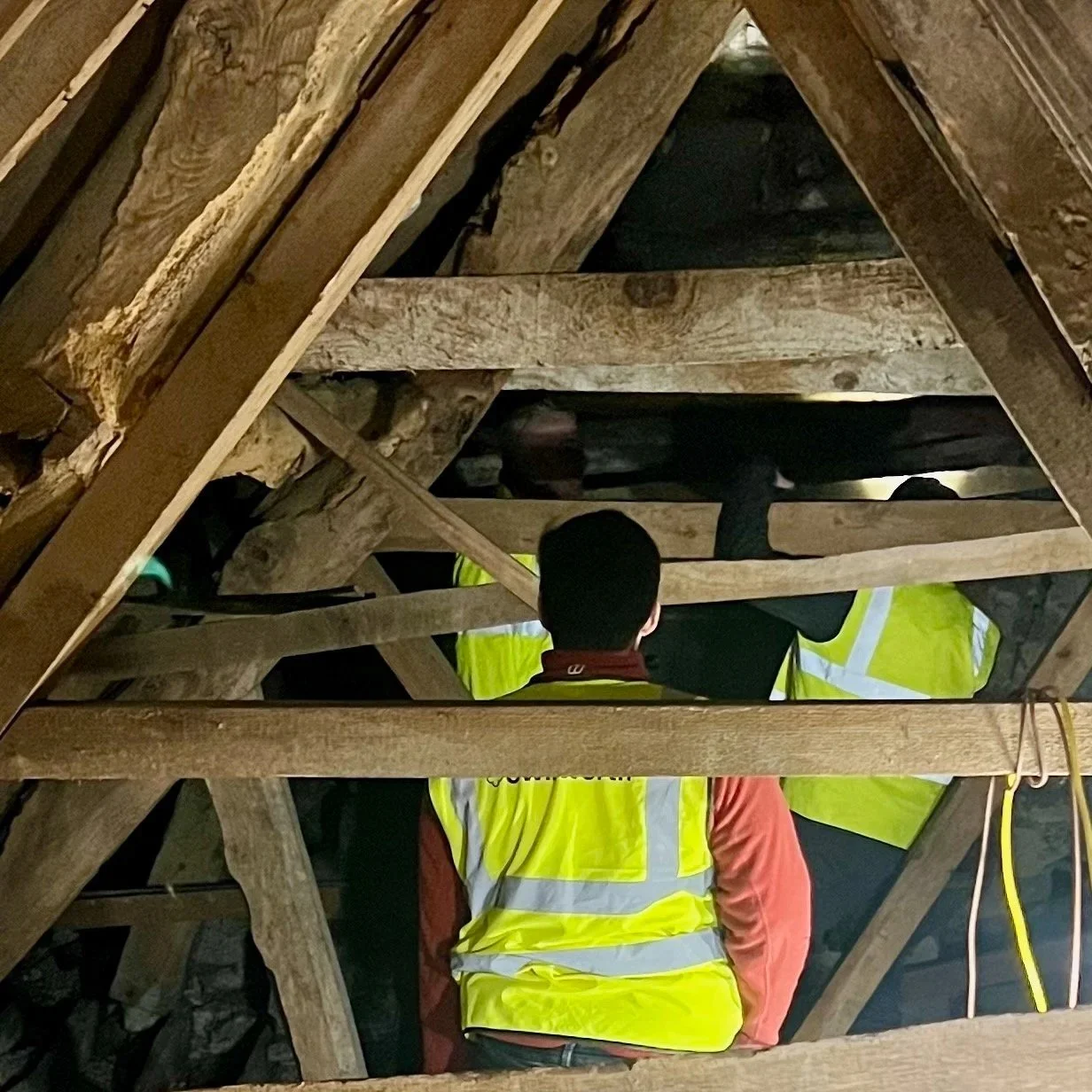 Construction workers wearing yellow safety vests working within a wooden attic framework.