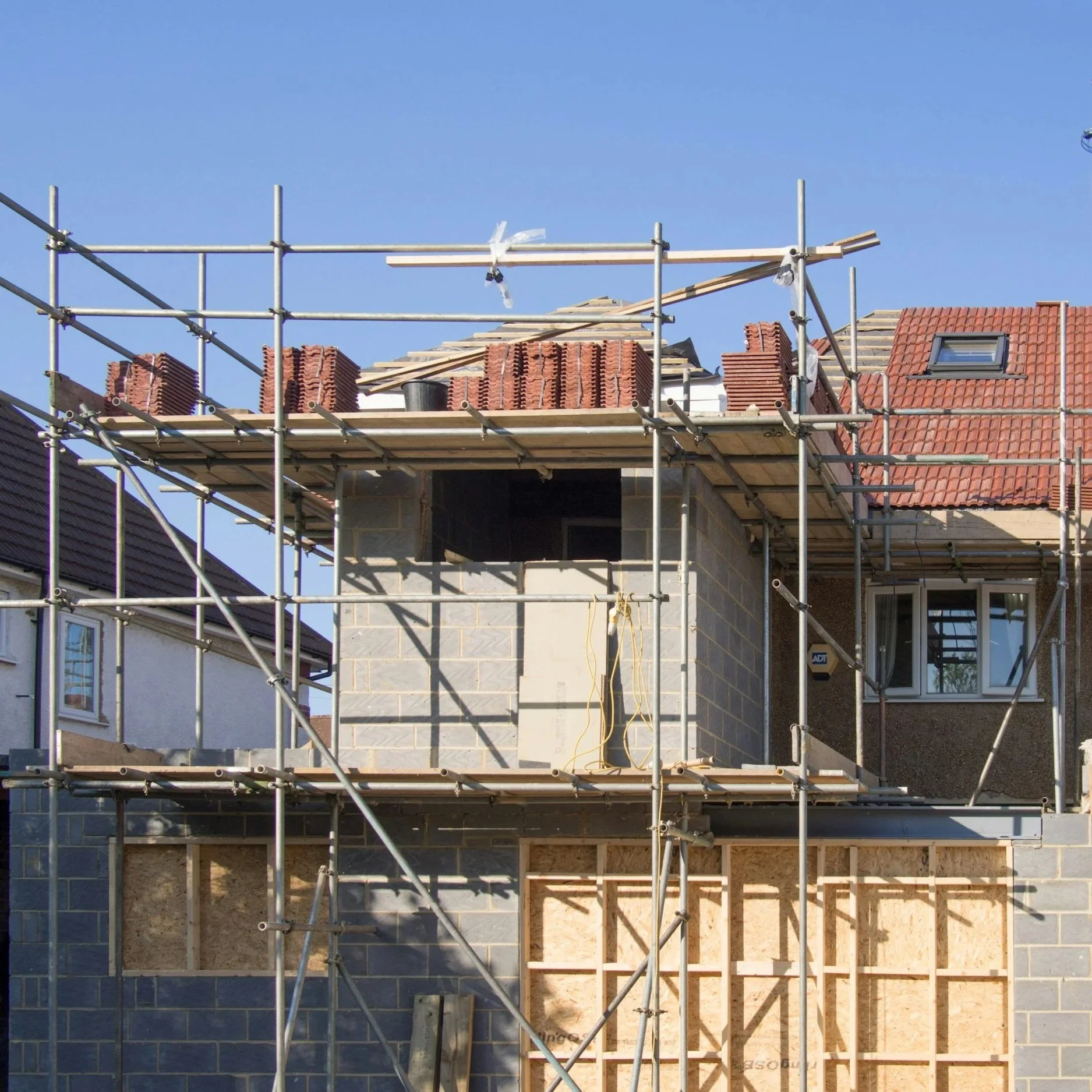 Under construction house with scaffolding, brick and concrete walls, and a clear blue sky.