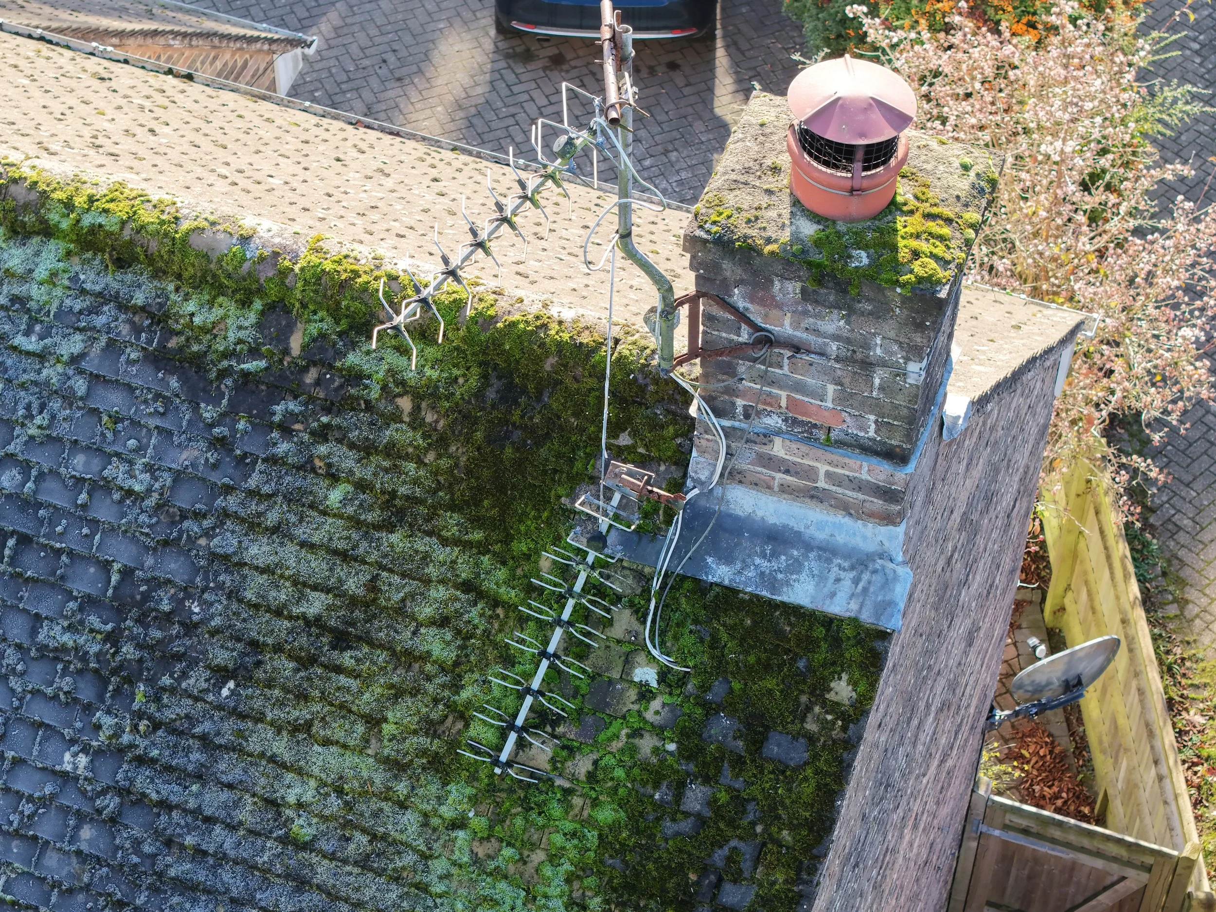 Bird's eye view of a moss-covered brick chimney with a red cap and an outdoor television antenna mounted on top captured during a property drone survey inspection