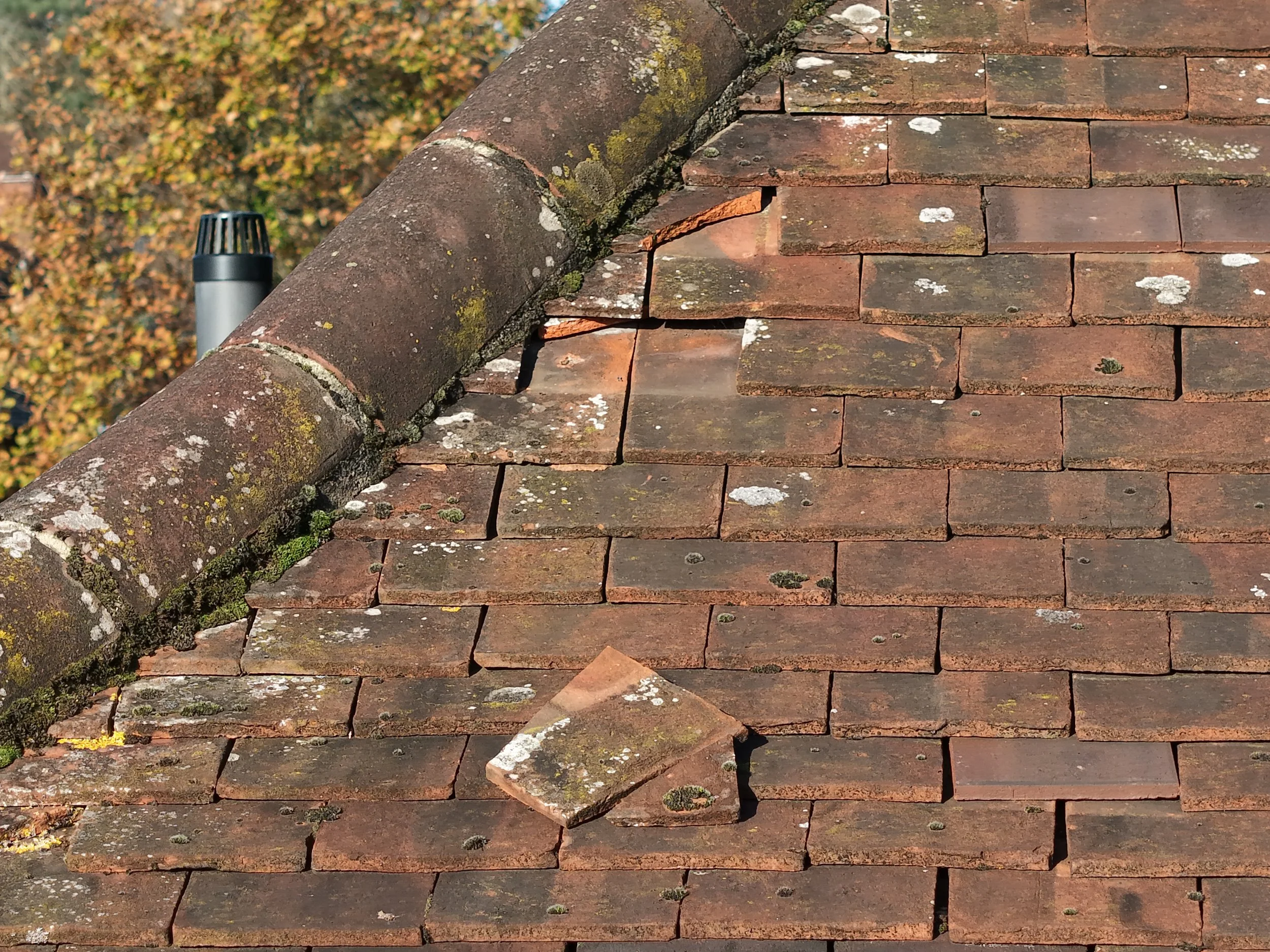 Close-up of a section of a sloped roof with red bricks, some of which are cracked or missing, and a piece of roof tile dislodged captured during a property drone survey inspection