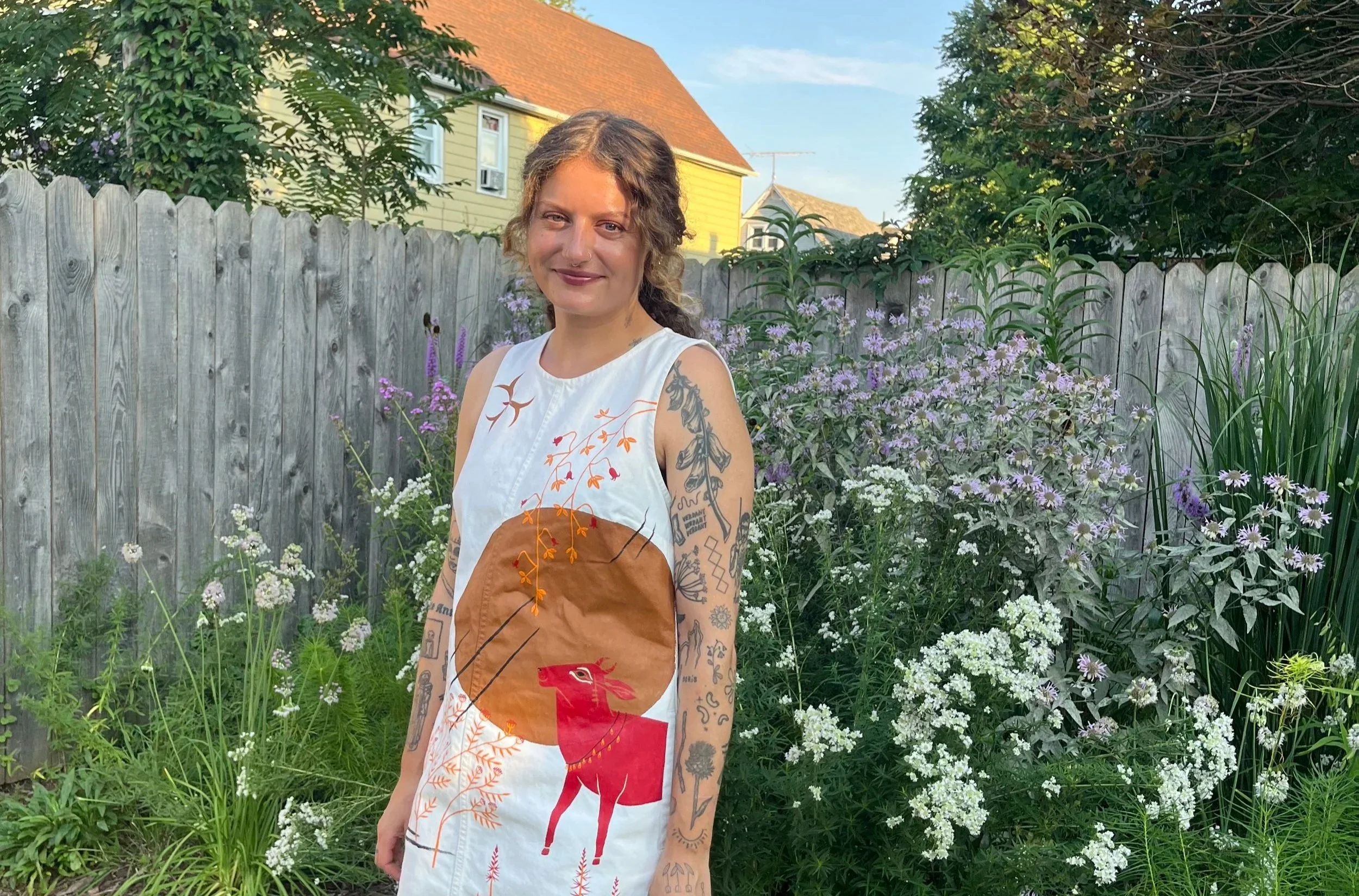 A woman artist and garden designer stands in garden in front of native plants.