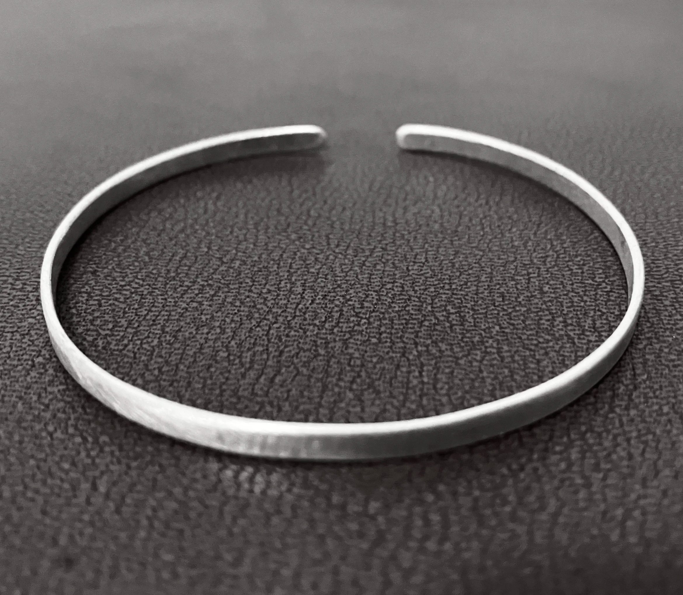Close-up of a minimalist ring with a small gap, placed on a textured leather surface.