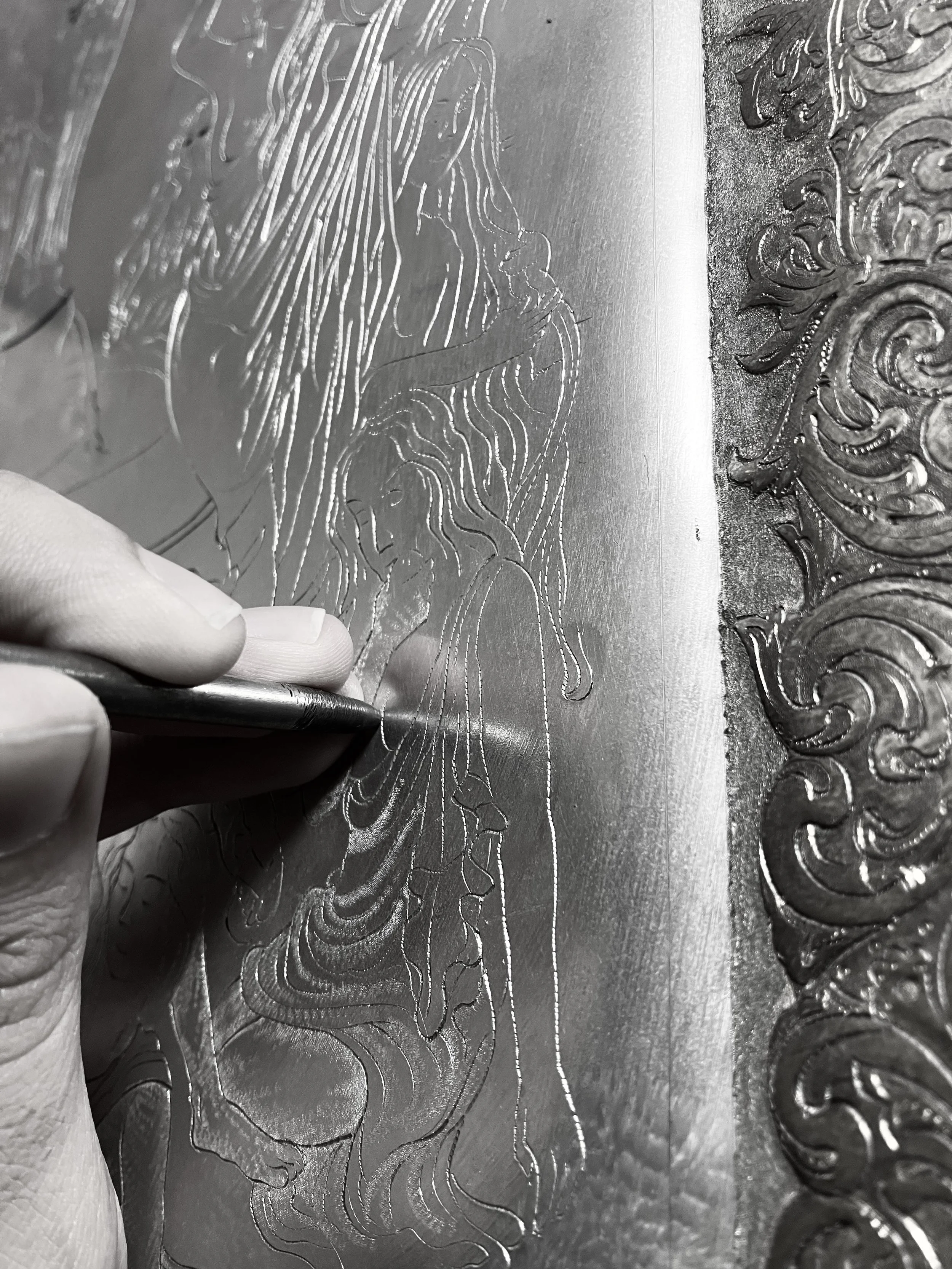 Hand holding a chisel to sculpt an unclothed girl on silver