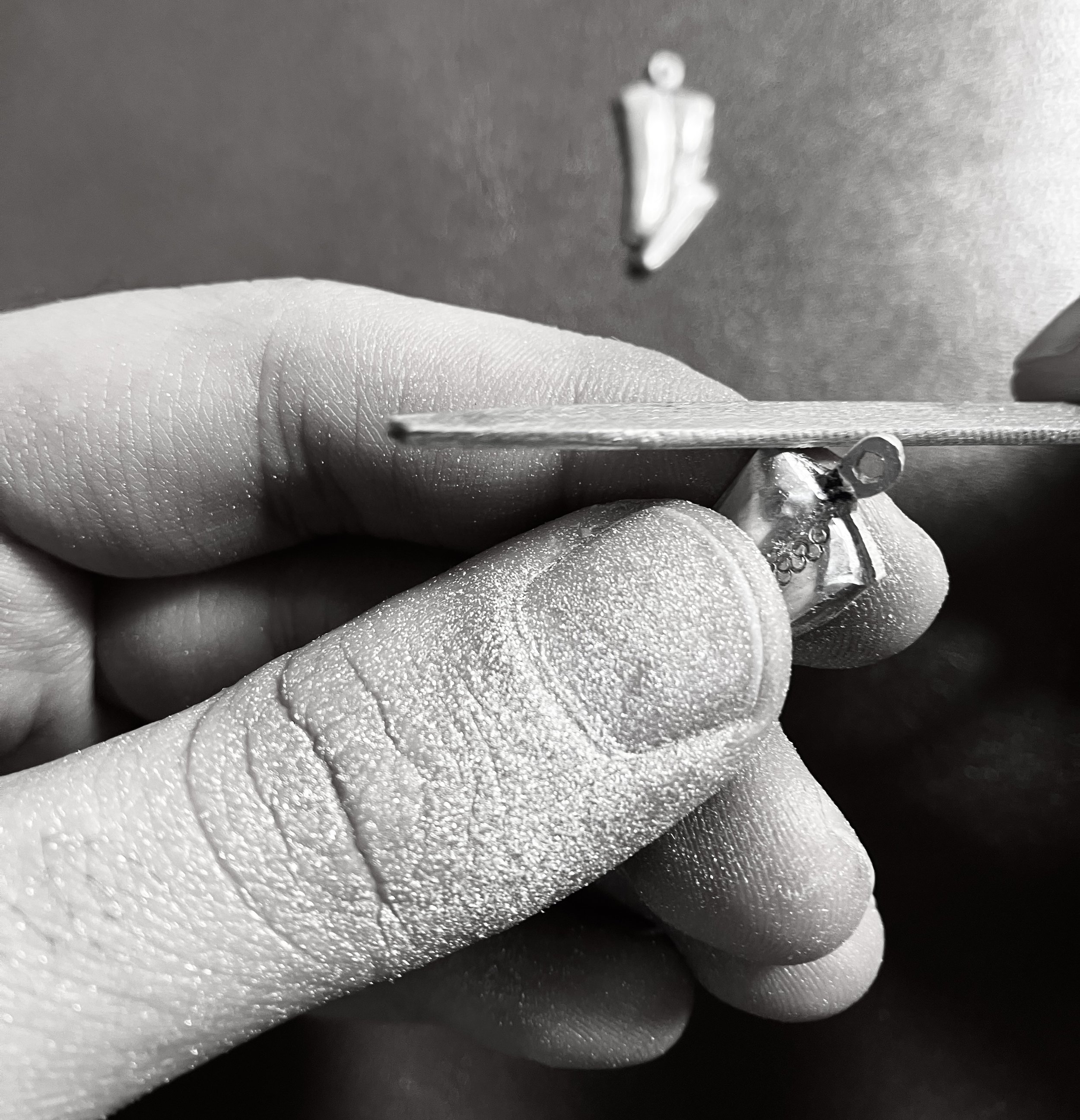 Artist's hands holding and filing silver earrings