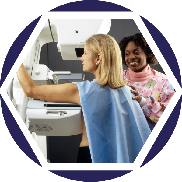 Eine Frau erhält eine Mammografie in einem medizinischen Untersuchungsraum, während eine Patientin neben ihr lächelnd zuschaut.