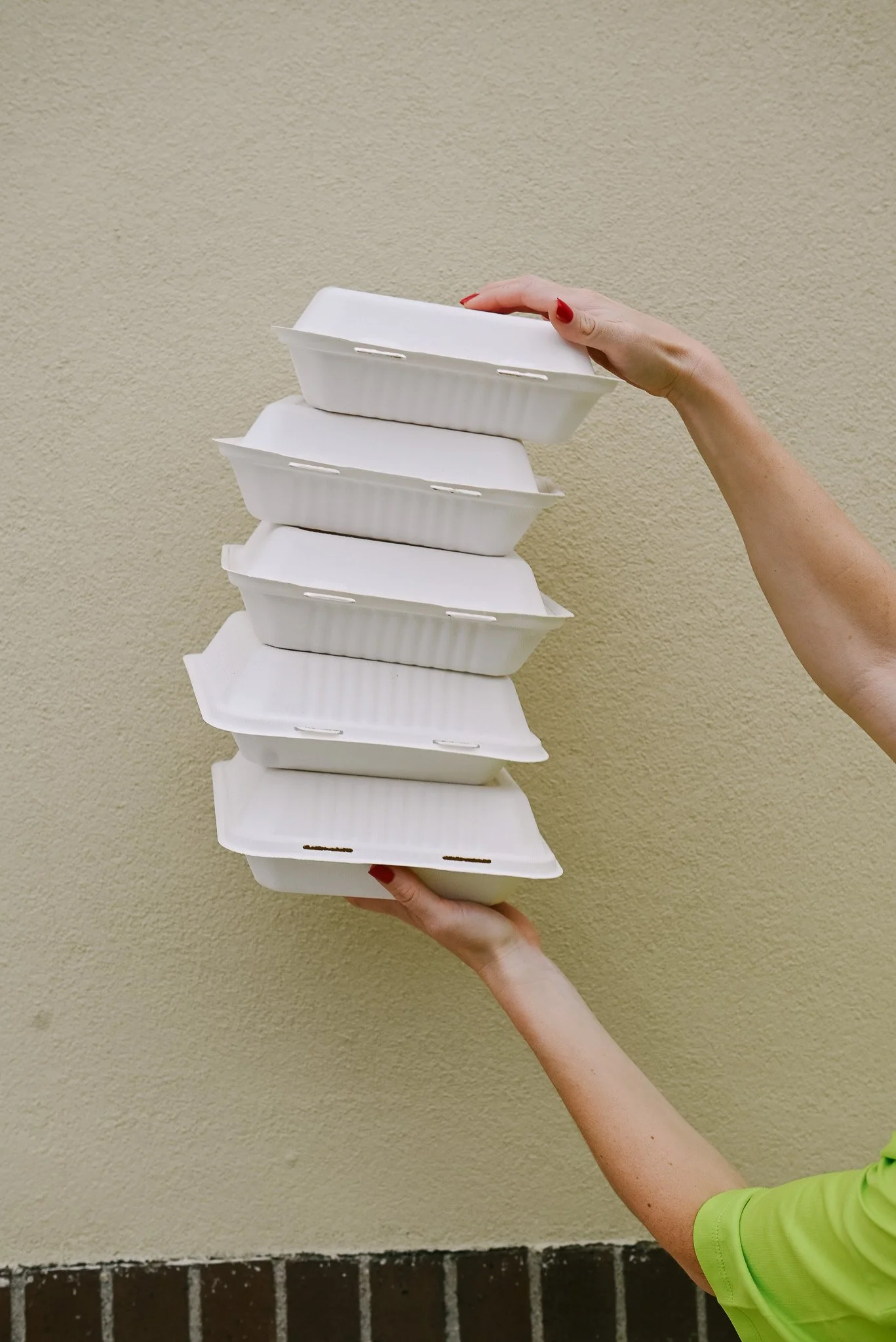 Hand holding a stack of five empty white foam food containers against a beige wall.