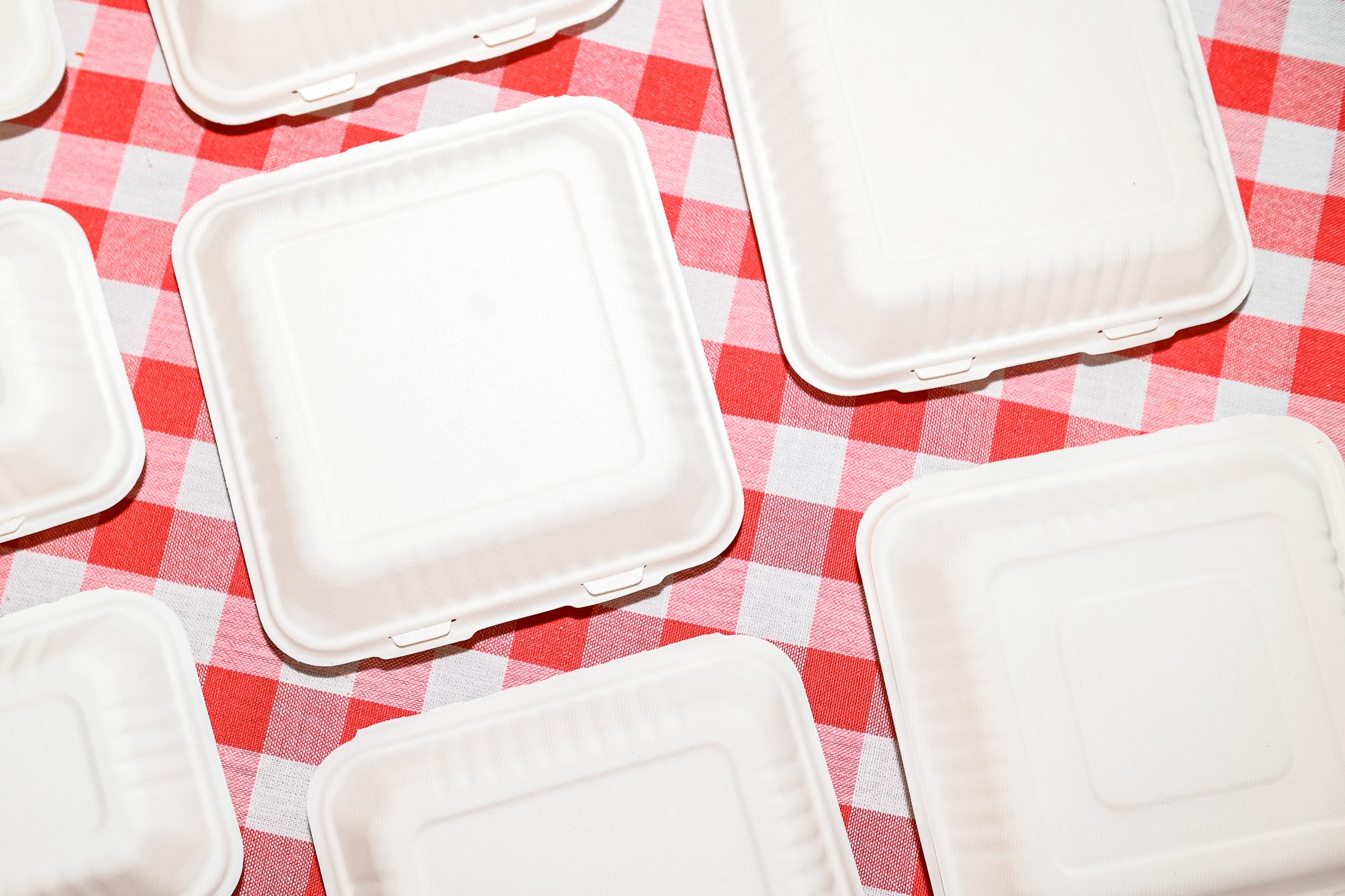Multiple empty white food containers on a red and white checkered tablecloth.