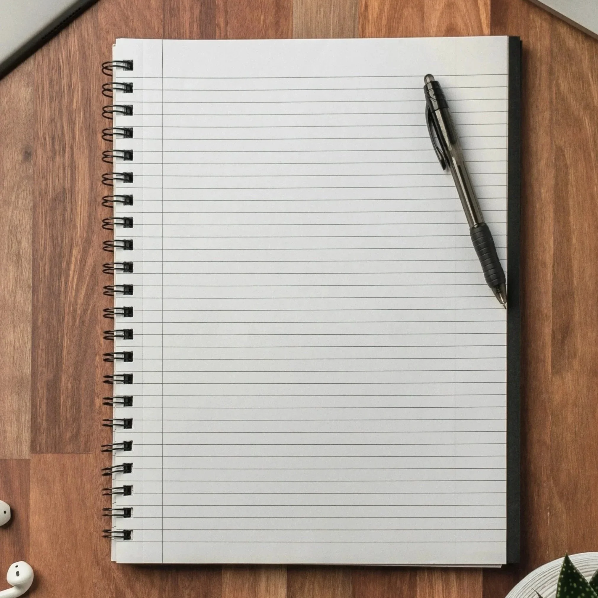 Open lined notebook with a black pen resting on it, placed on a wooden desk.