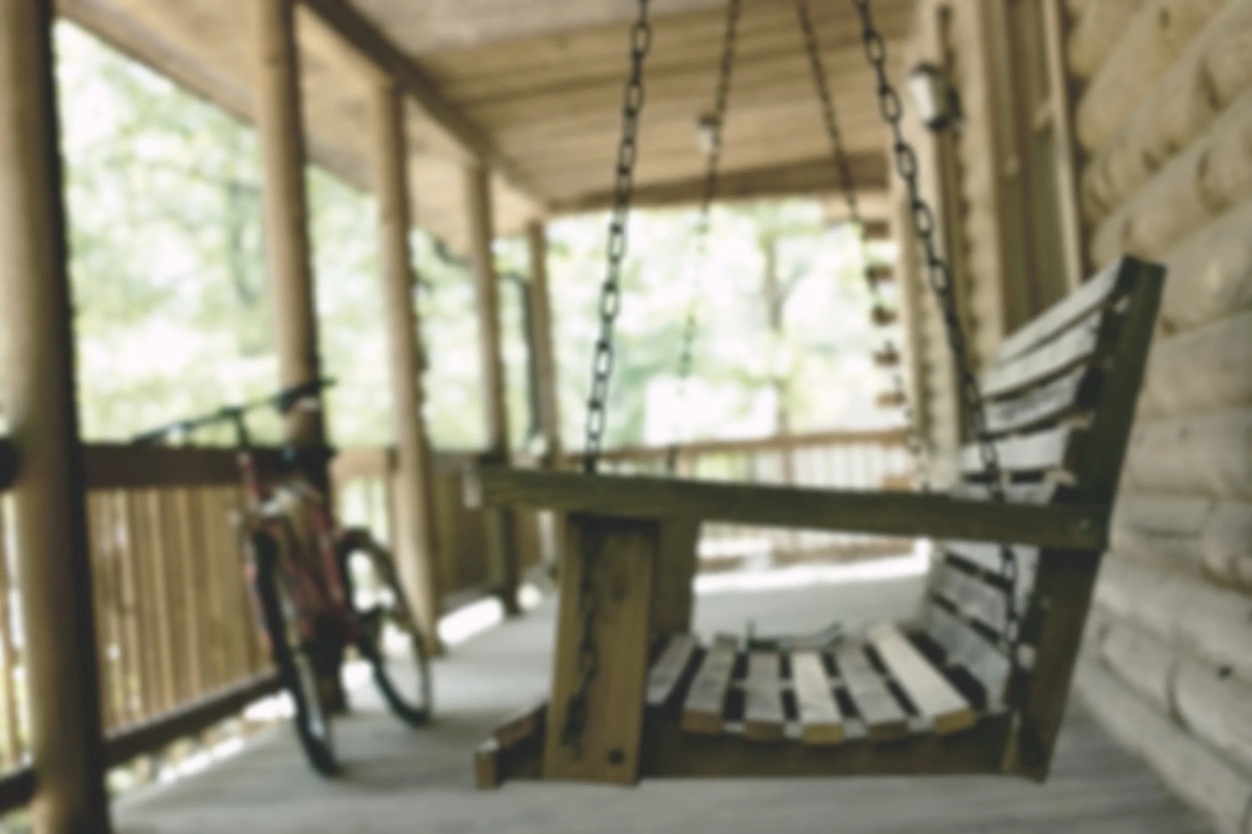 A wooden porch with a swing and a bicycle in the background.