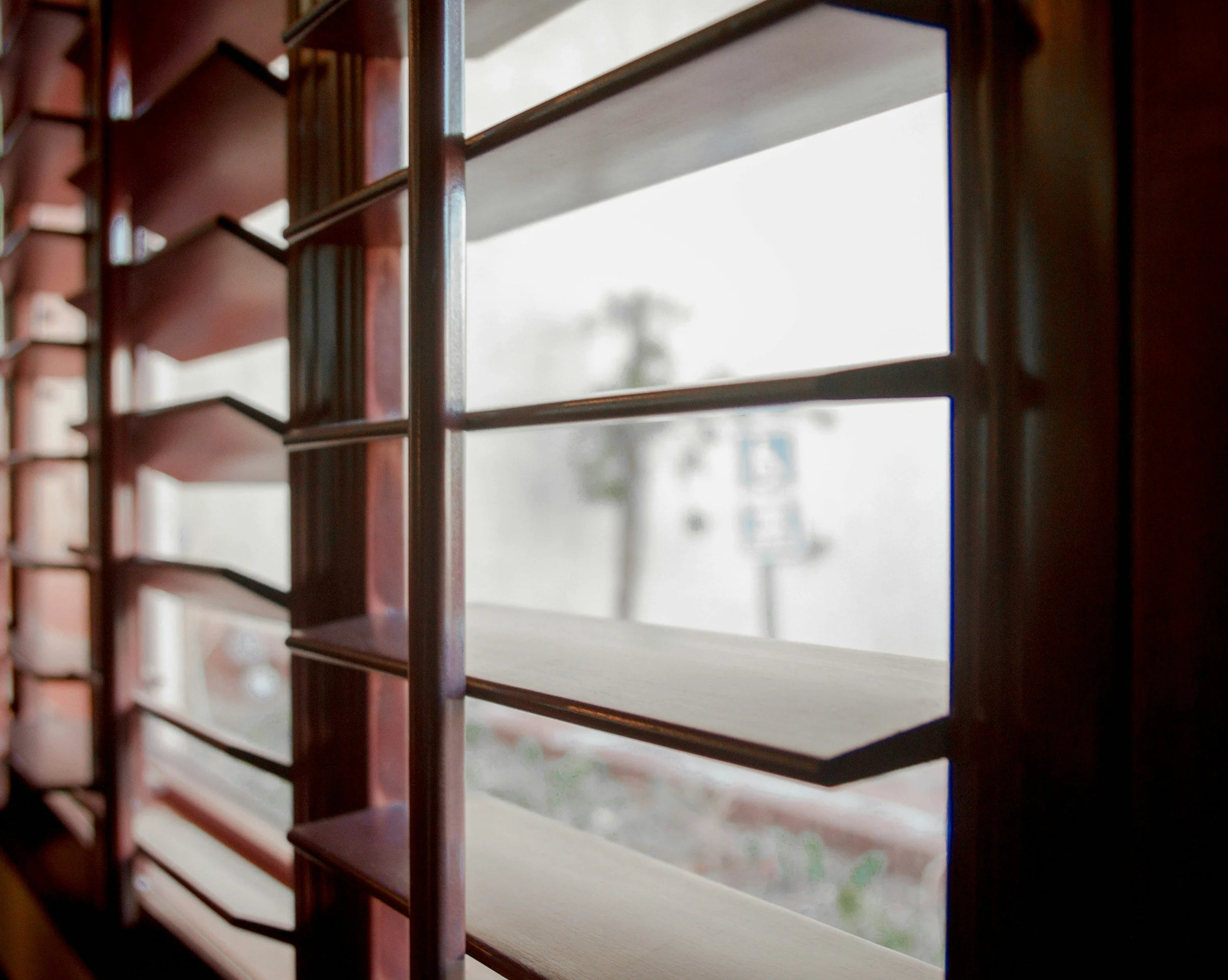 Close-up of wooden window shutters with open blinds, showing the outside blurred view of trees and sky.