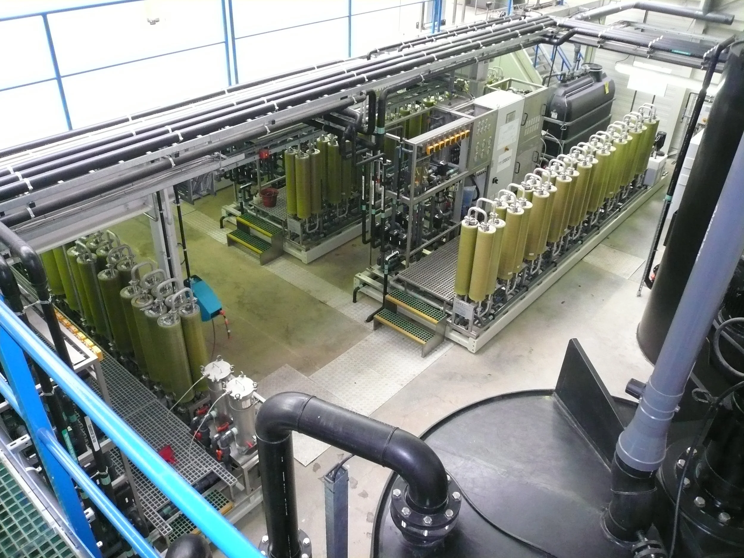 Industrial machinery with large green cylinders arranged in rows, pipes, and control panels in a factory setting.