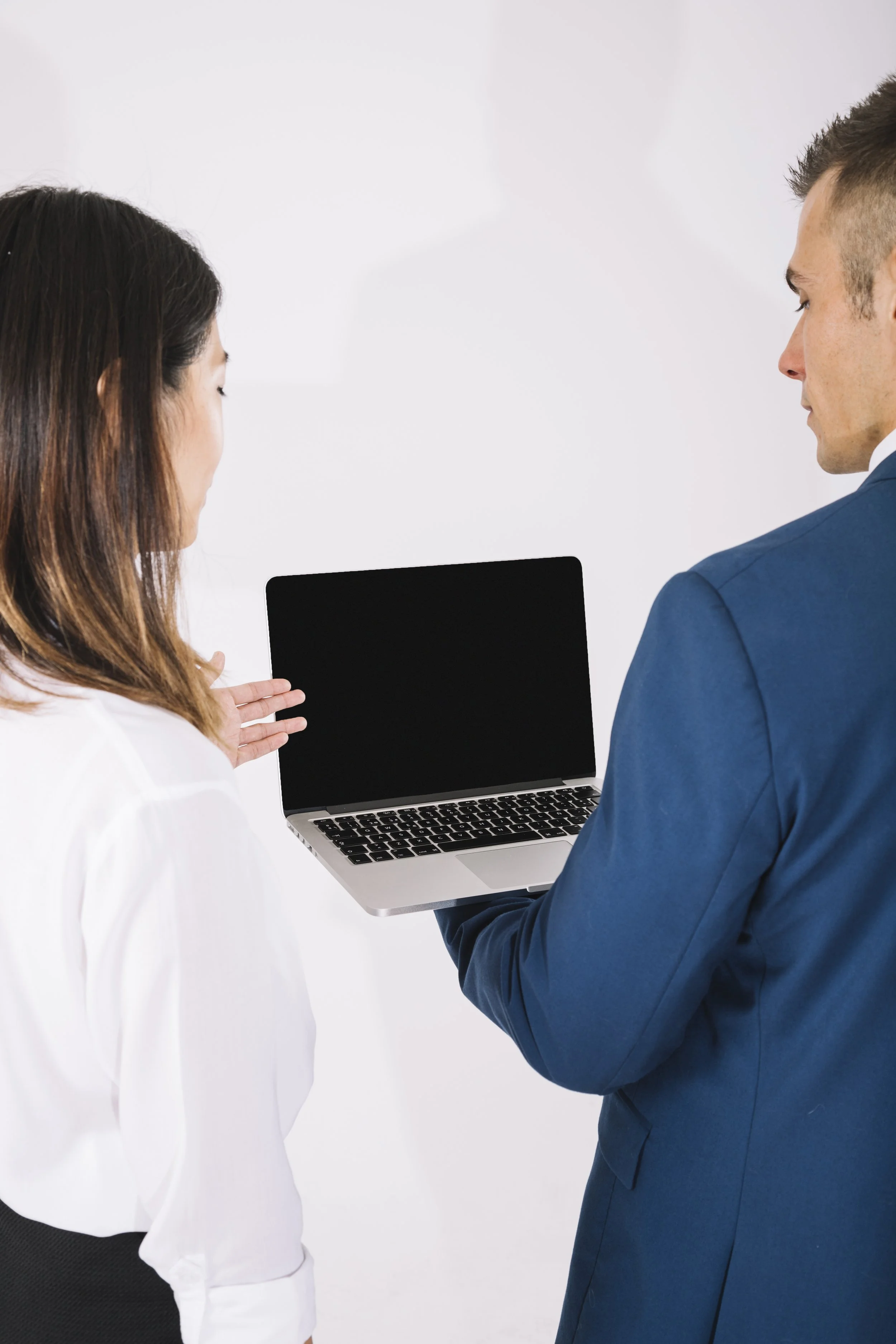 Two professionals in a conversation, one woman and one man, with the man holding a laptop with a black screen.