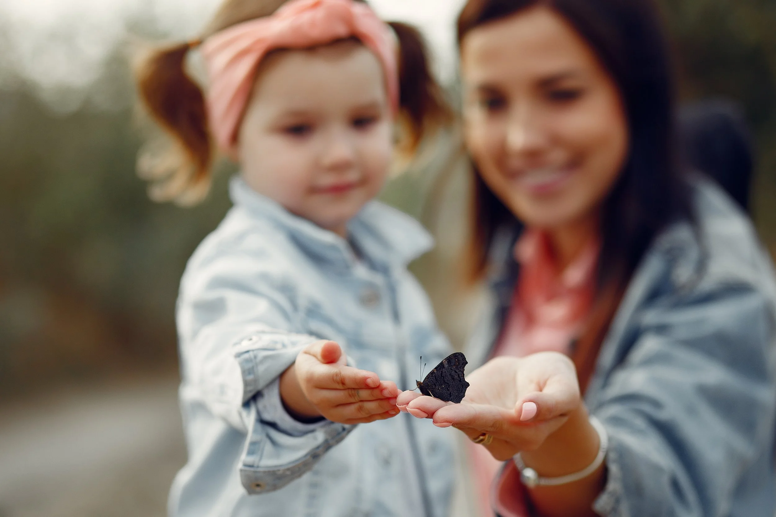 A woman and a young girl holding a black butterfly together outdoors.