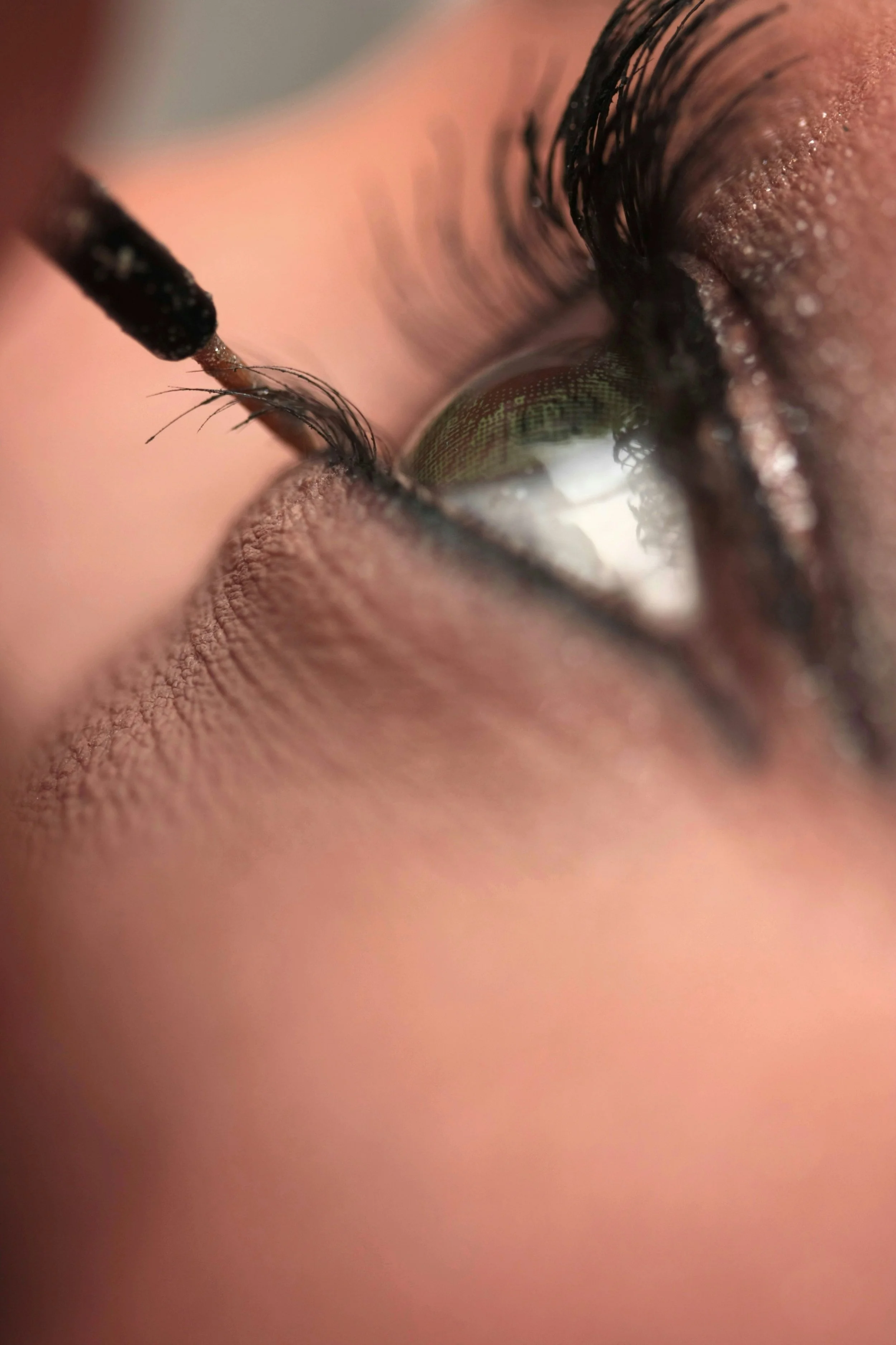 Close-up of a person's eye with makeup and long eyelashes, as a makeup brush applies eyeliner.