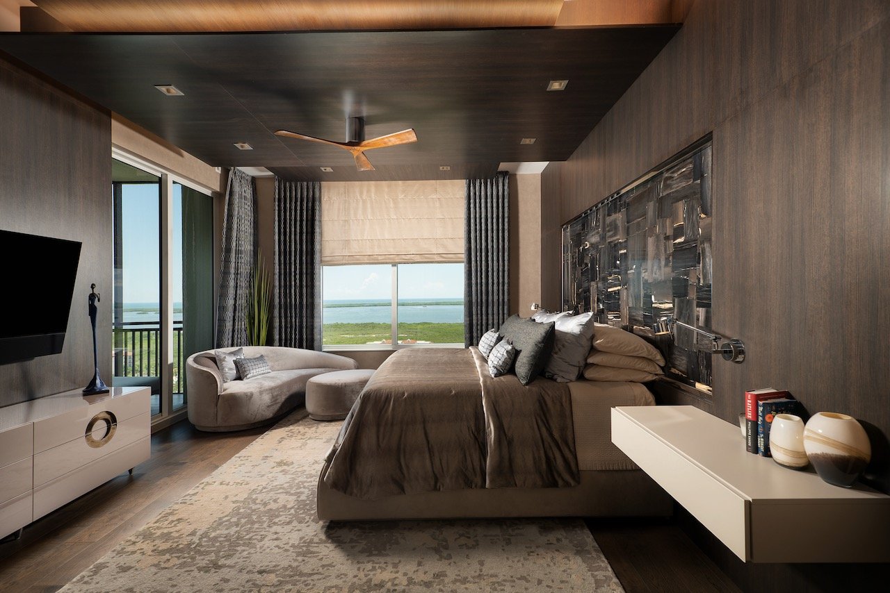 Modern Penthouse primary bedroom with dark ceiling treatment, curved sofa, large-scale artwork and Gulf water views — Gloria Black Design Fort Myers Florida