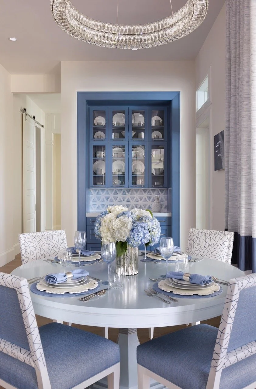 New England Charmer breakfast nook by Gloria Black Design antique blue china cabinet with glass display crystal chandelier, round pedestal dining table with upholstered chairs blue and white color story award-winning interior design Naples Florida