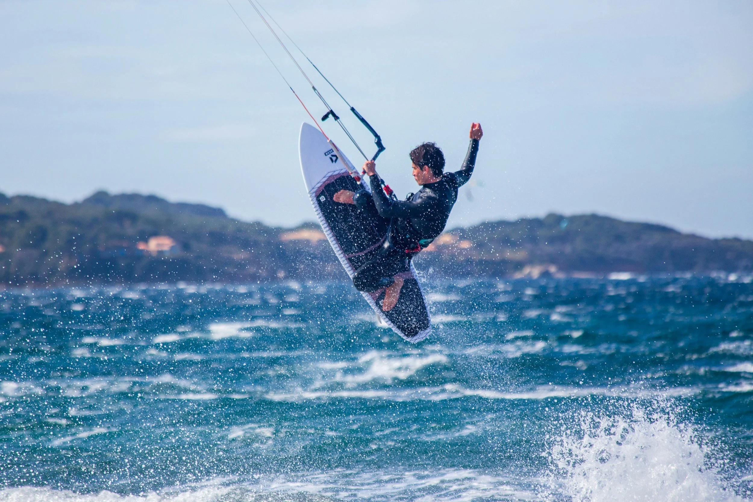 A person engaged in windsurfing on the ocean, holding onto a sail with a backdrop of hills and a sky.