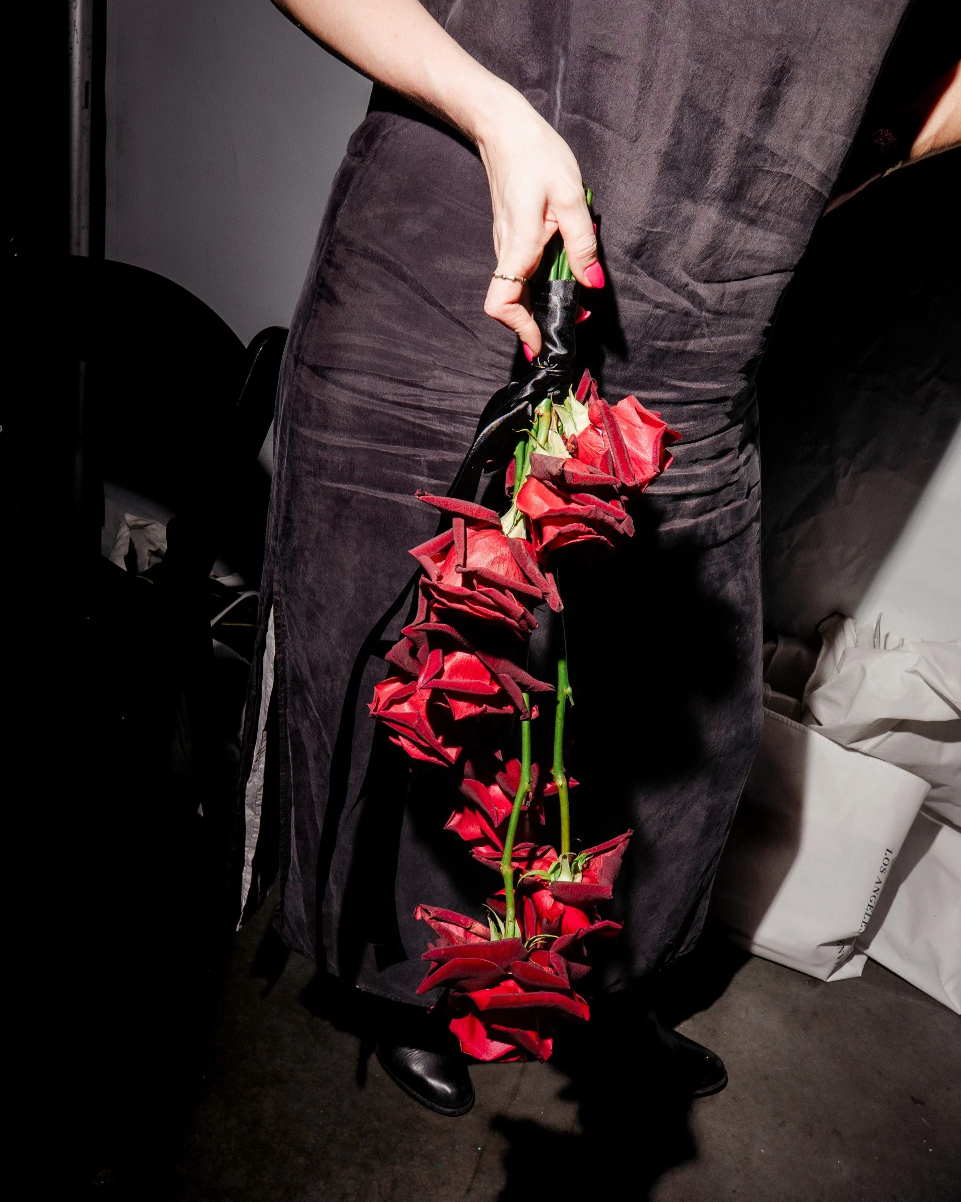 Person holding a black bag with red roses attached, standing on a dark carpeted floor.