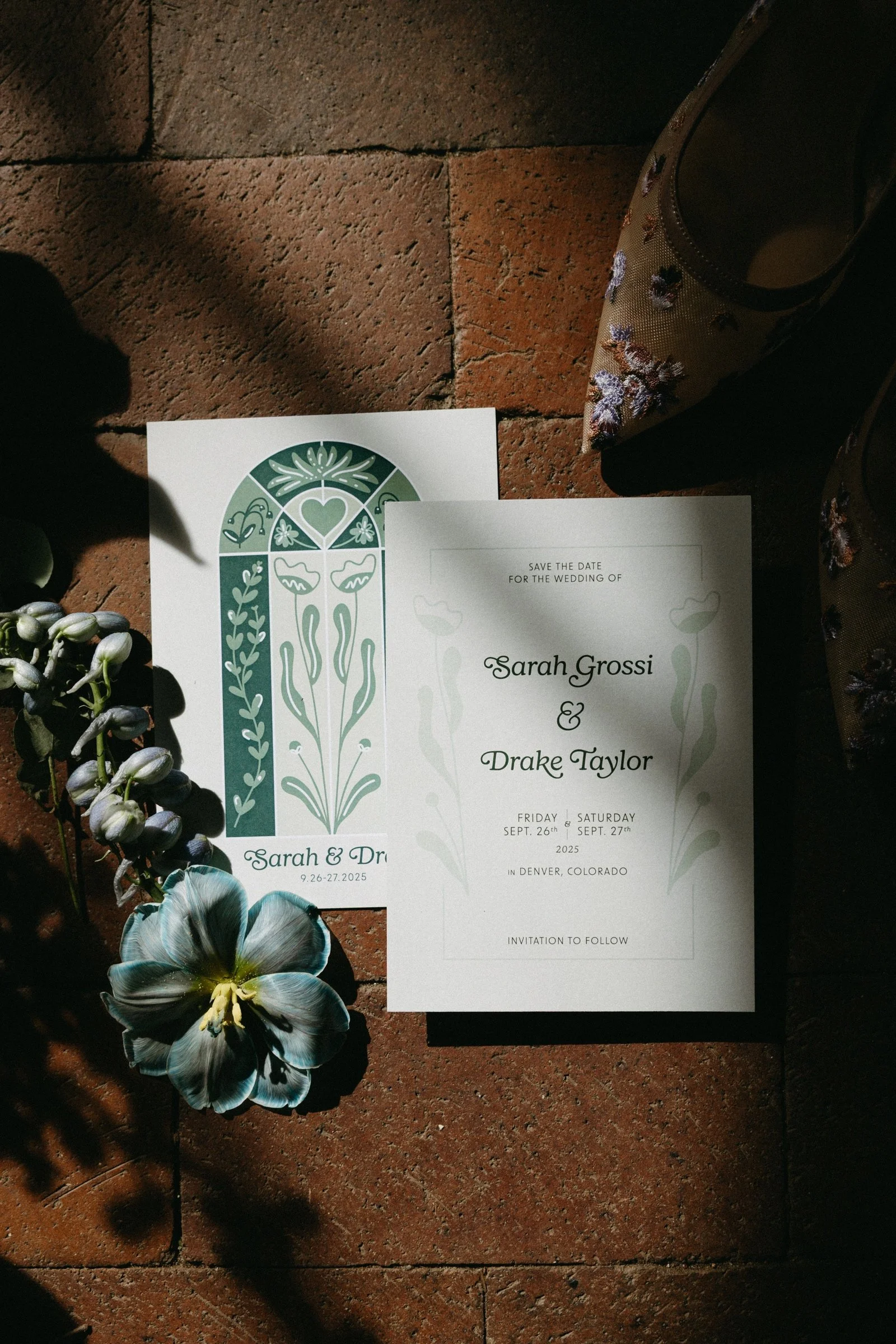 Wedding save the date and invitation cards with floral and heart designs, a flower, and a pair of embroidered shoes on a brick floor.