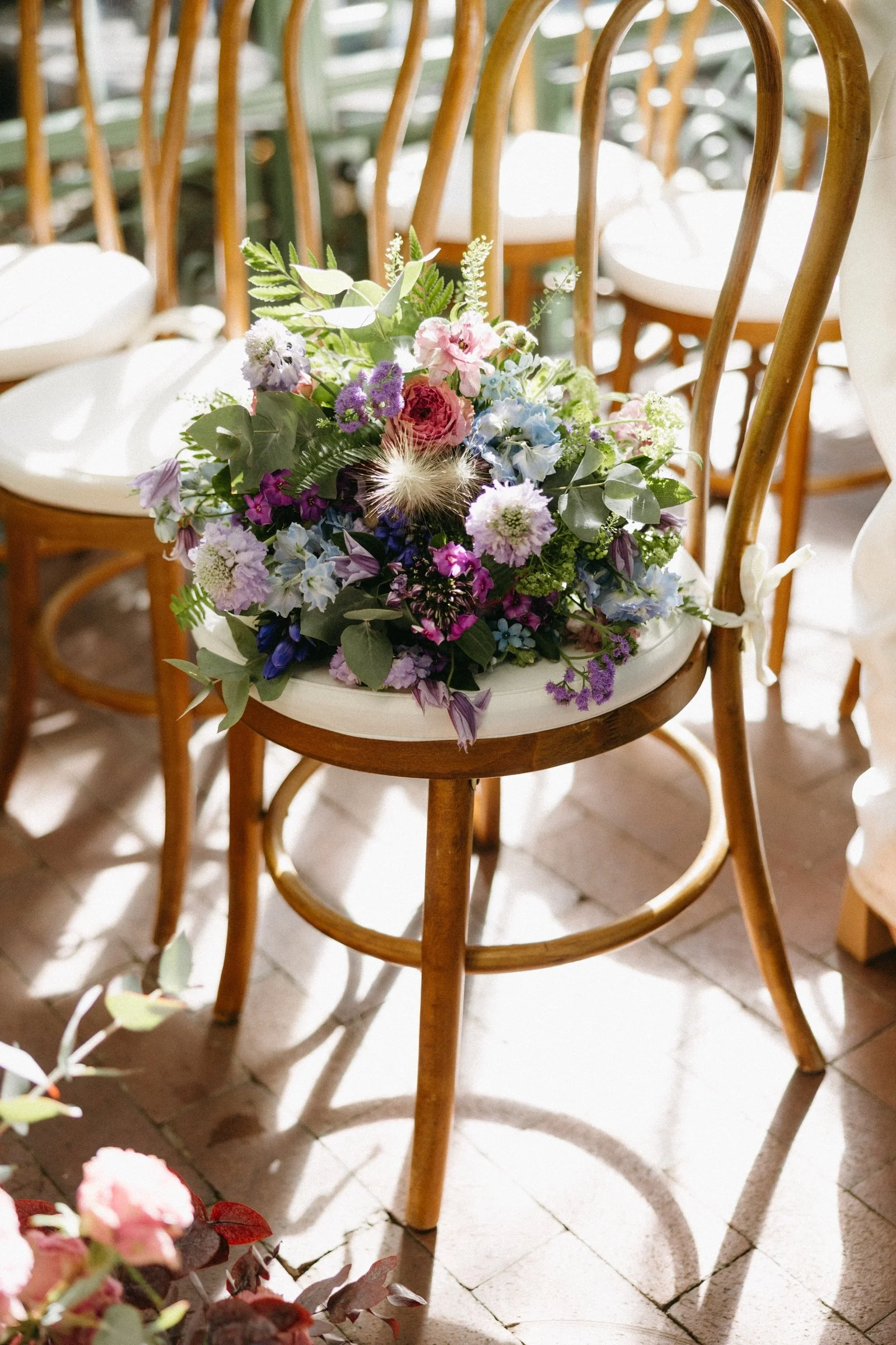 A bouquet of mixed flowers on a wooden chair with white cushion in a well-lit indoor setting.