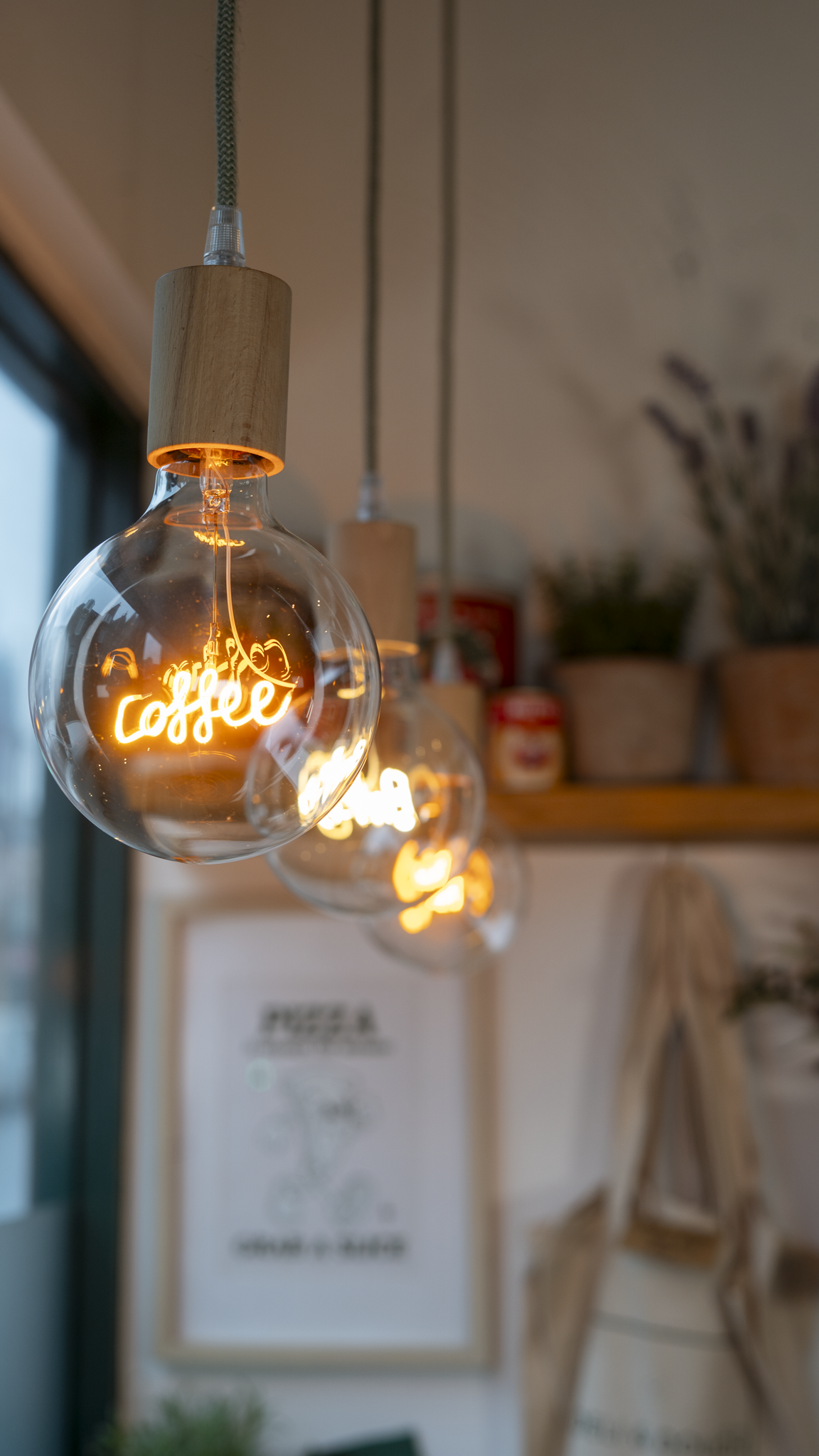 Three hanging light bulbs with wooden sockets, each with a glowing neon sign inside that says "coffee" in cursive, in a cozy interior setting.