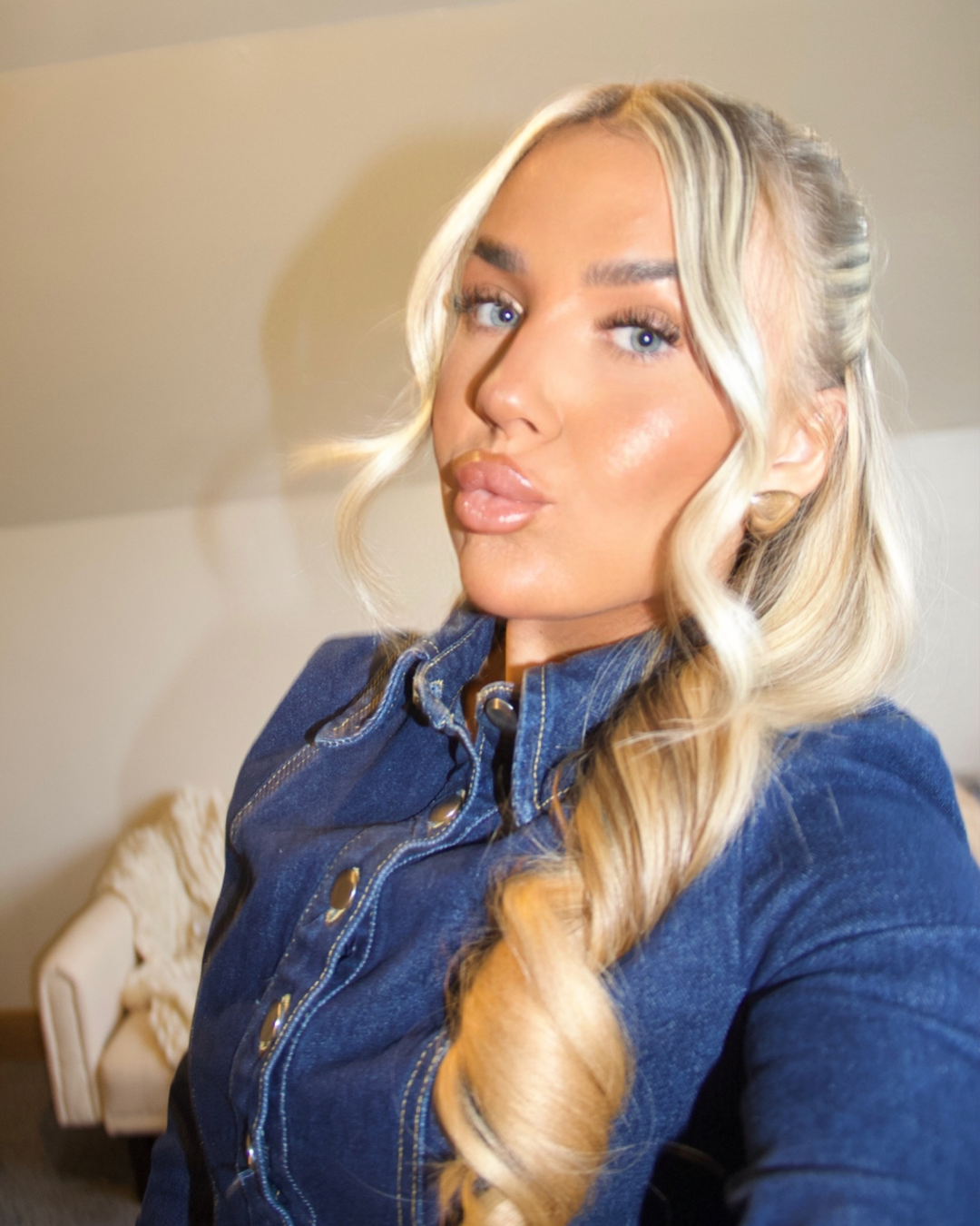 Close-up of a woman with long, curly blonde hair, wearing a denim jacket, taking a selfie