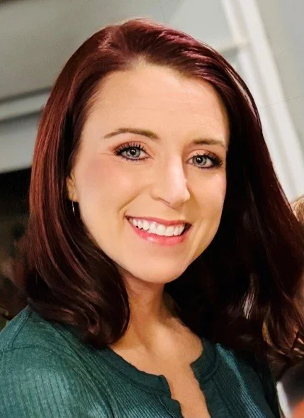 A woman with shoulder-length red hair smiling at the camera.