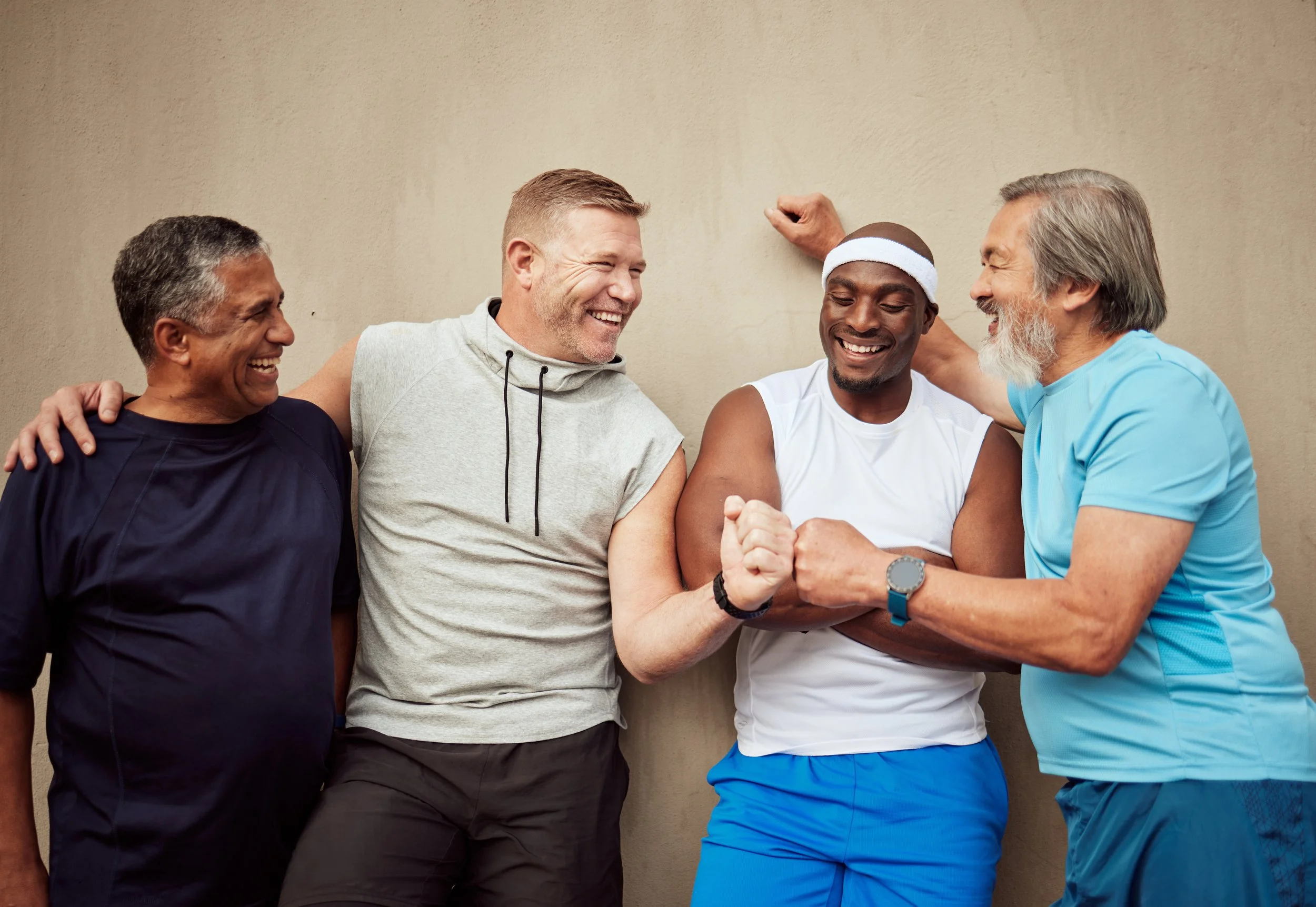 Four men smiling, with two of them shaking hands in front of a beige wall.