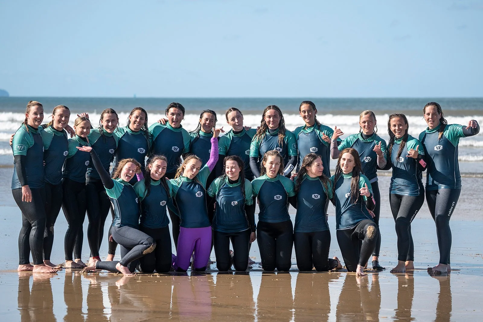 Group of women in wetsuits on the beach with waves in the background.