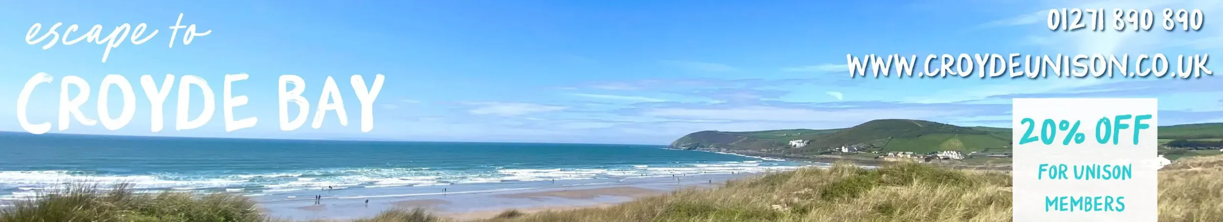 A scenic view of Croyde Bay with sandy beach, ocean waves, grassy dunes, and hills in the background on a clear day.