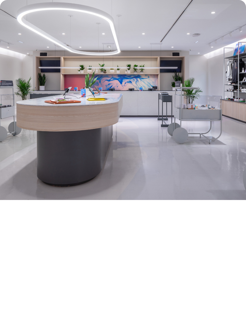 Modern retail store with a curved marble checkout counter, green plants, and a geometric ceiling light fixture, displaying merchandise and digital tablets.