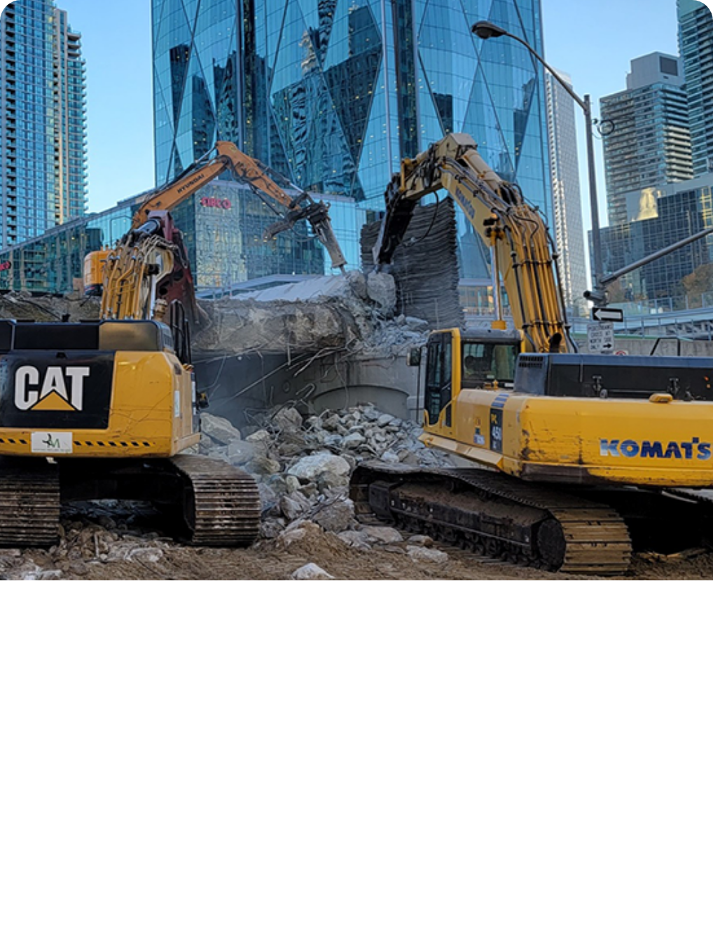 Construction site with excavators demolishing a building in an urban area with tall glass buildings in the background.
