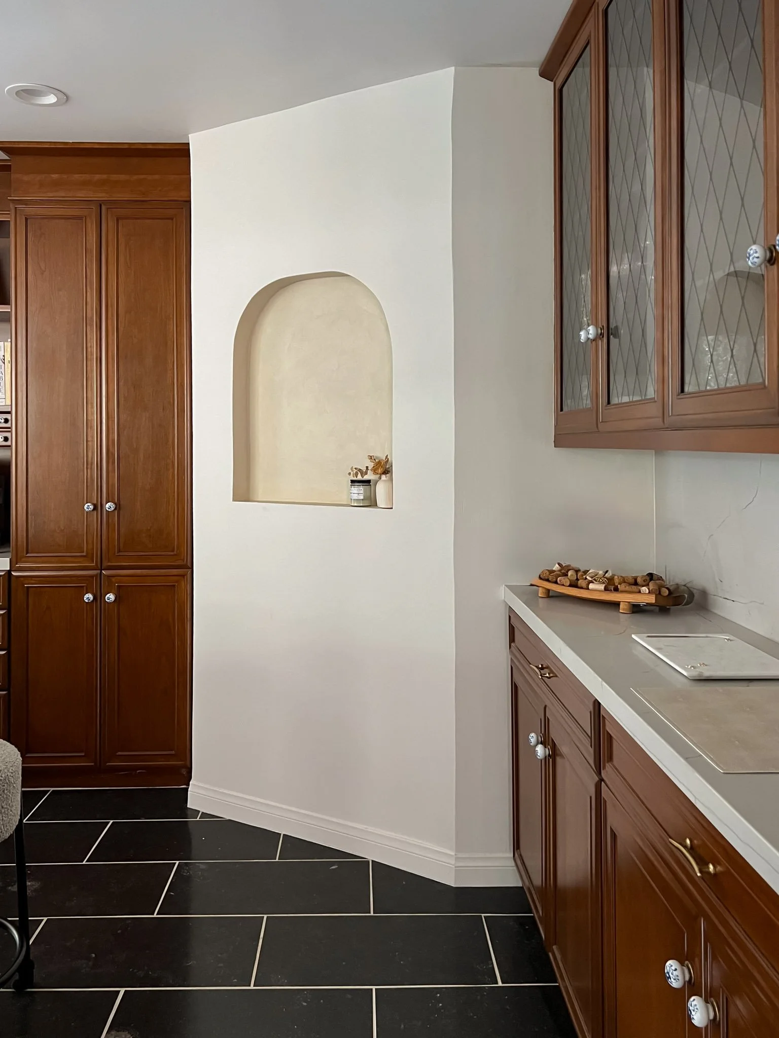 Kitchen with dark tile flooring, wooden cabinets, and a small recessed shelf in a white wall.