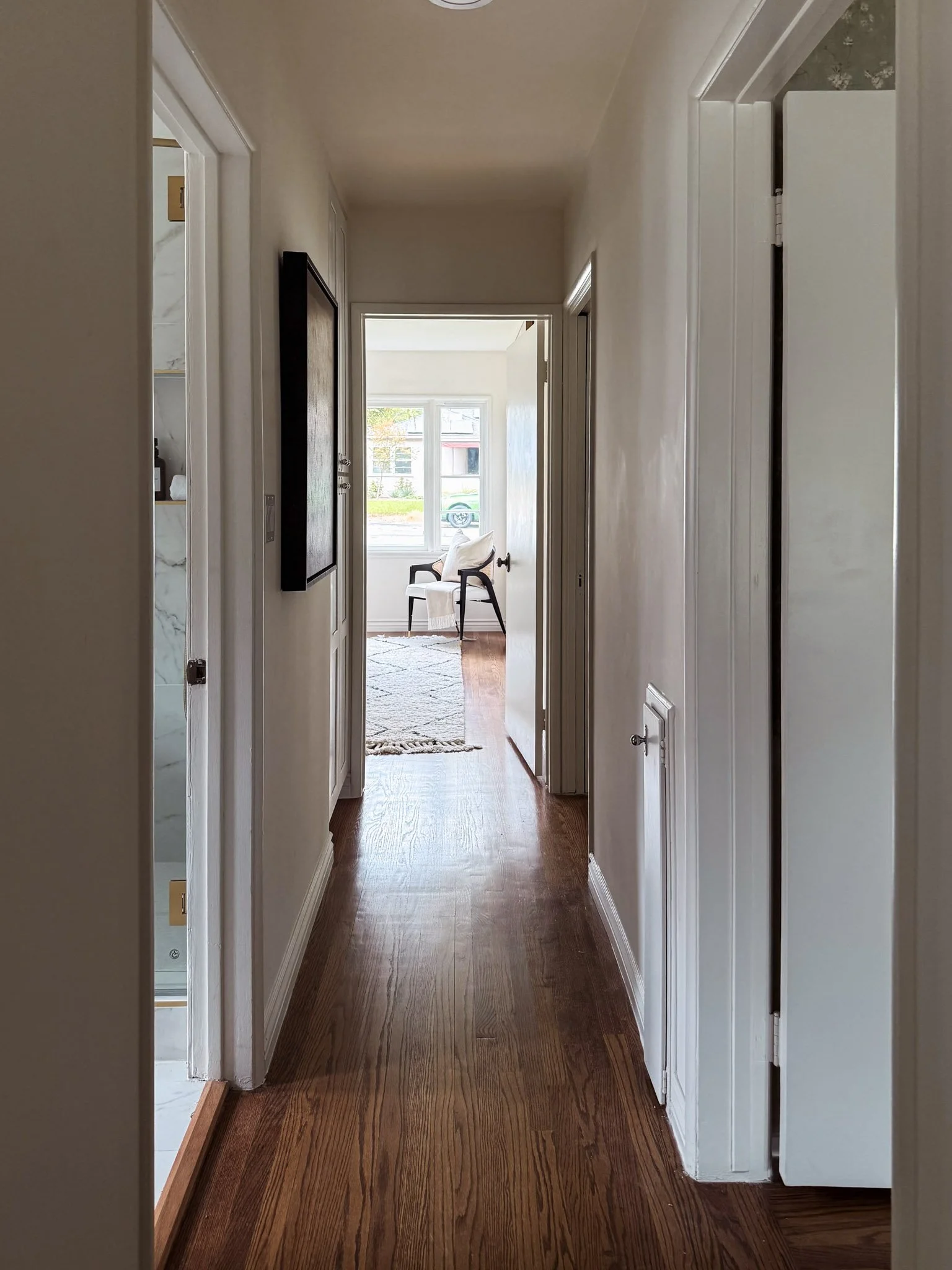 Interior view of a hallway leading to a bright room with a window and a chair.