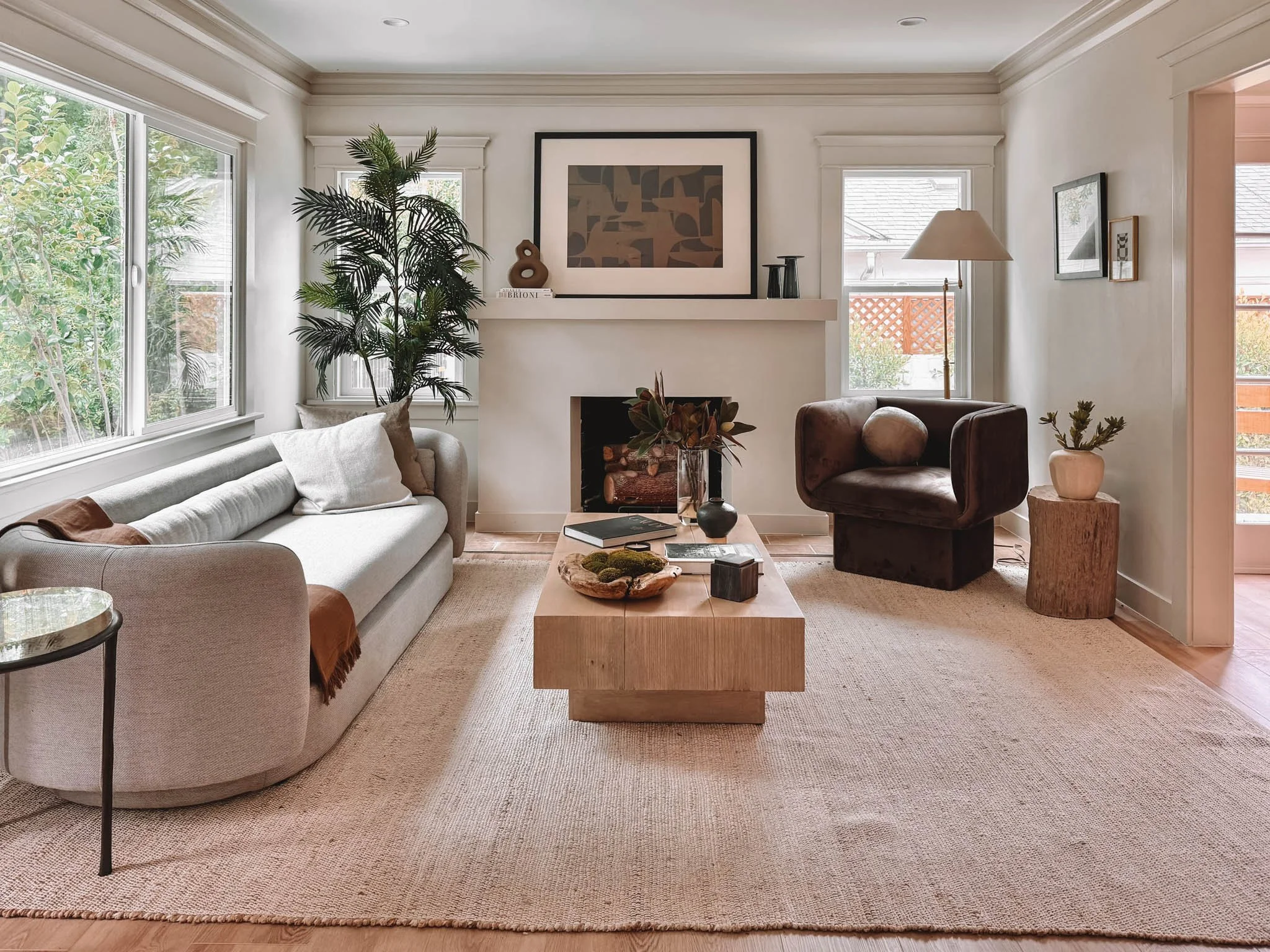 Living room with beige sofa, black armchair, wooden coffee table, fireplace, large windows, and various decorative items.
