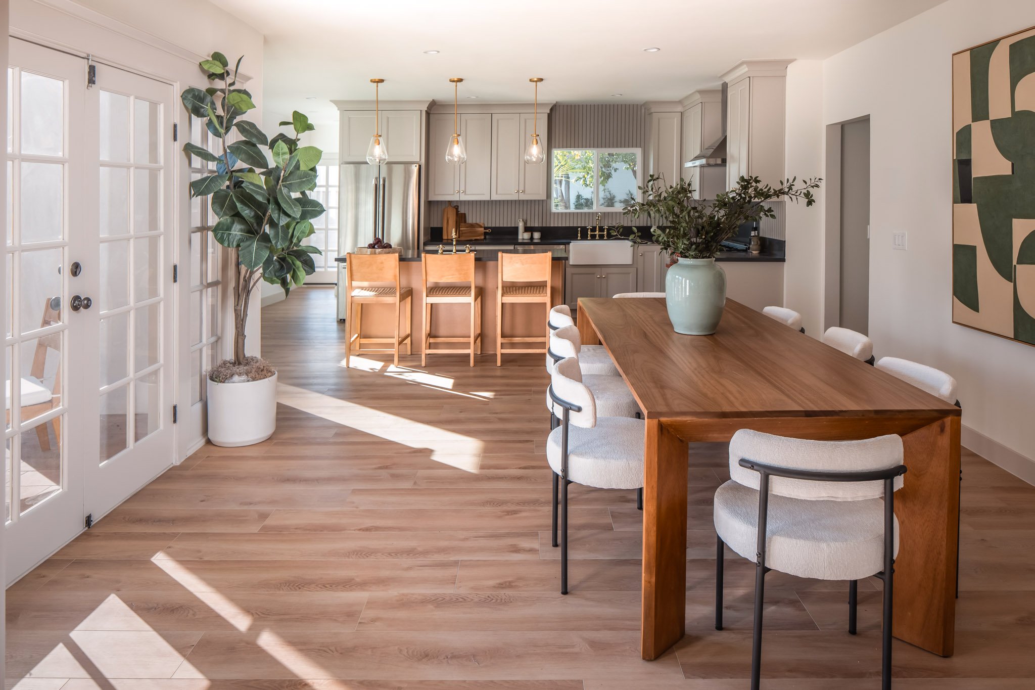 Open-concept dining and kitchen area with wooden table and chairs, potted plants, and natural sunlight.