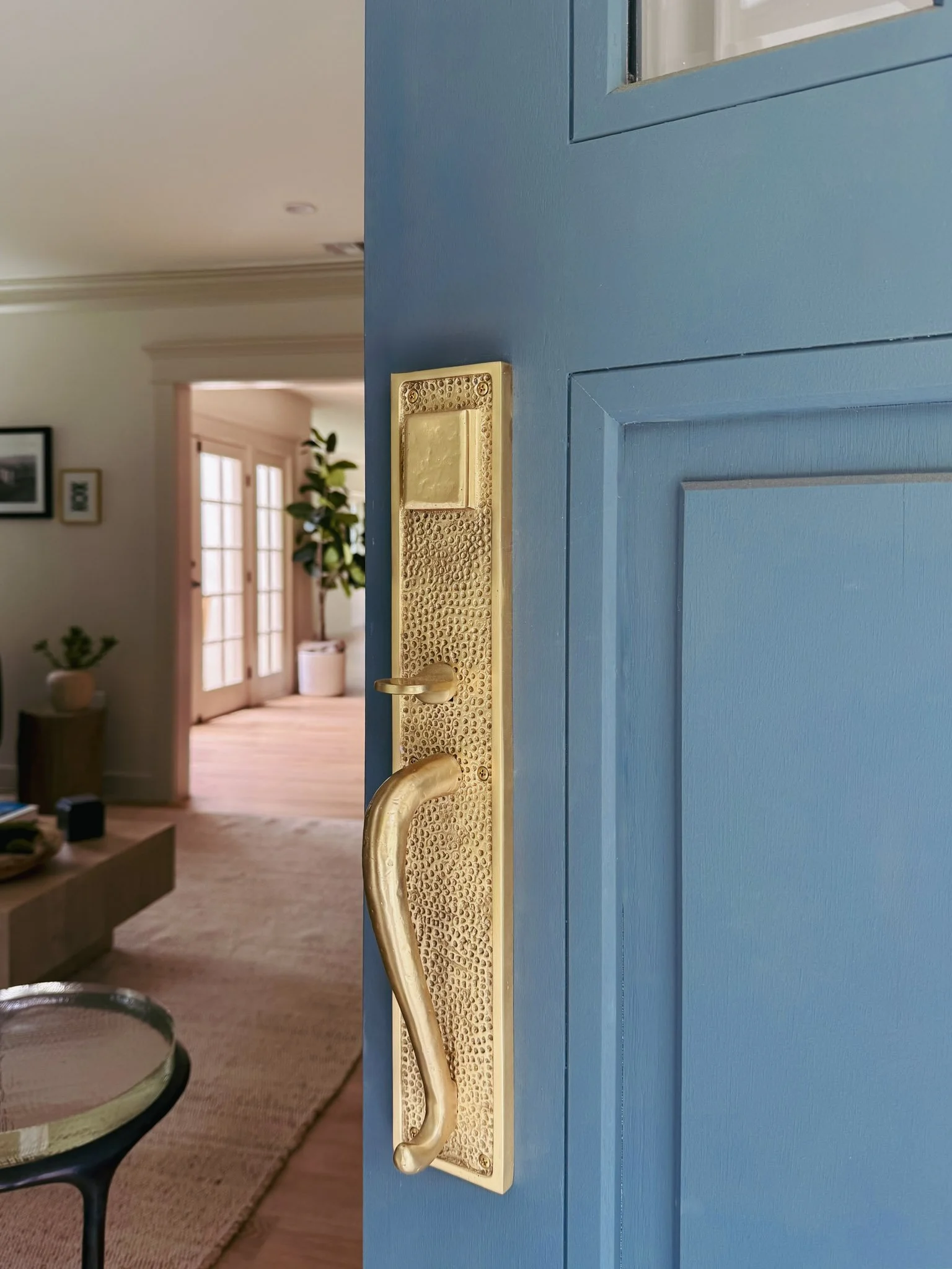 Close-up of a blue door with a gold-colored handle and lock, partially open inside a home with a living room visible in the background.