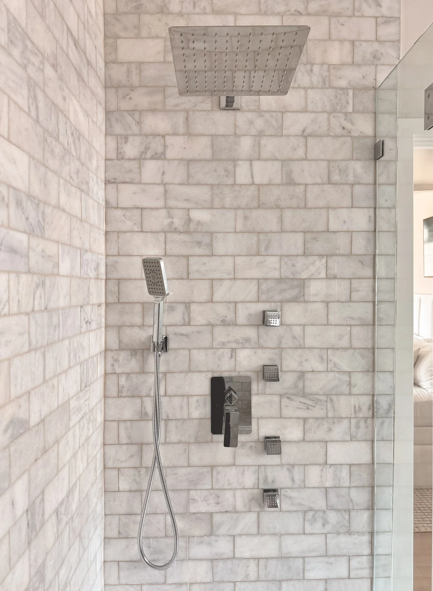Modern shower with large square rain shower head and four smaller square body spray jets on tiled wall, handheld shower head on adjustable holder.