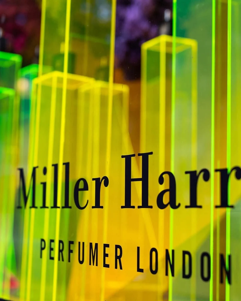Close-up of yellow and green neon-lit architecture with the text "Miller Harris PERFUMER LONDON" displayed.