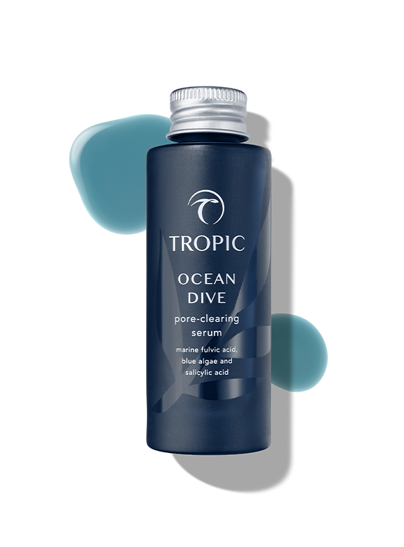A blue bottle of Tropic Ocean Dive pore-clearing serum with two blue-green droplet-like splashes in the background.