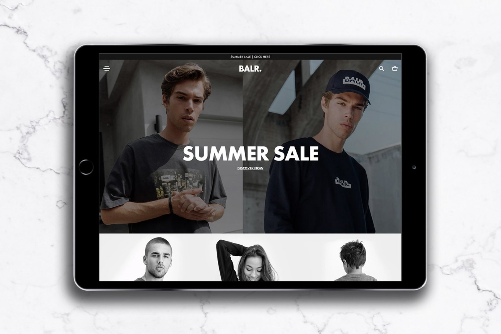 Tablet displaying a website with a summer sale promotion featuring models wearing casual clothing and accessories, set against an outdoor urban background.