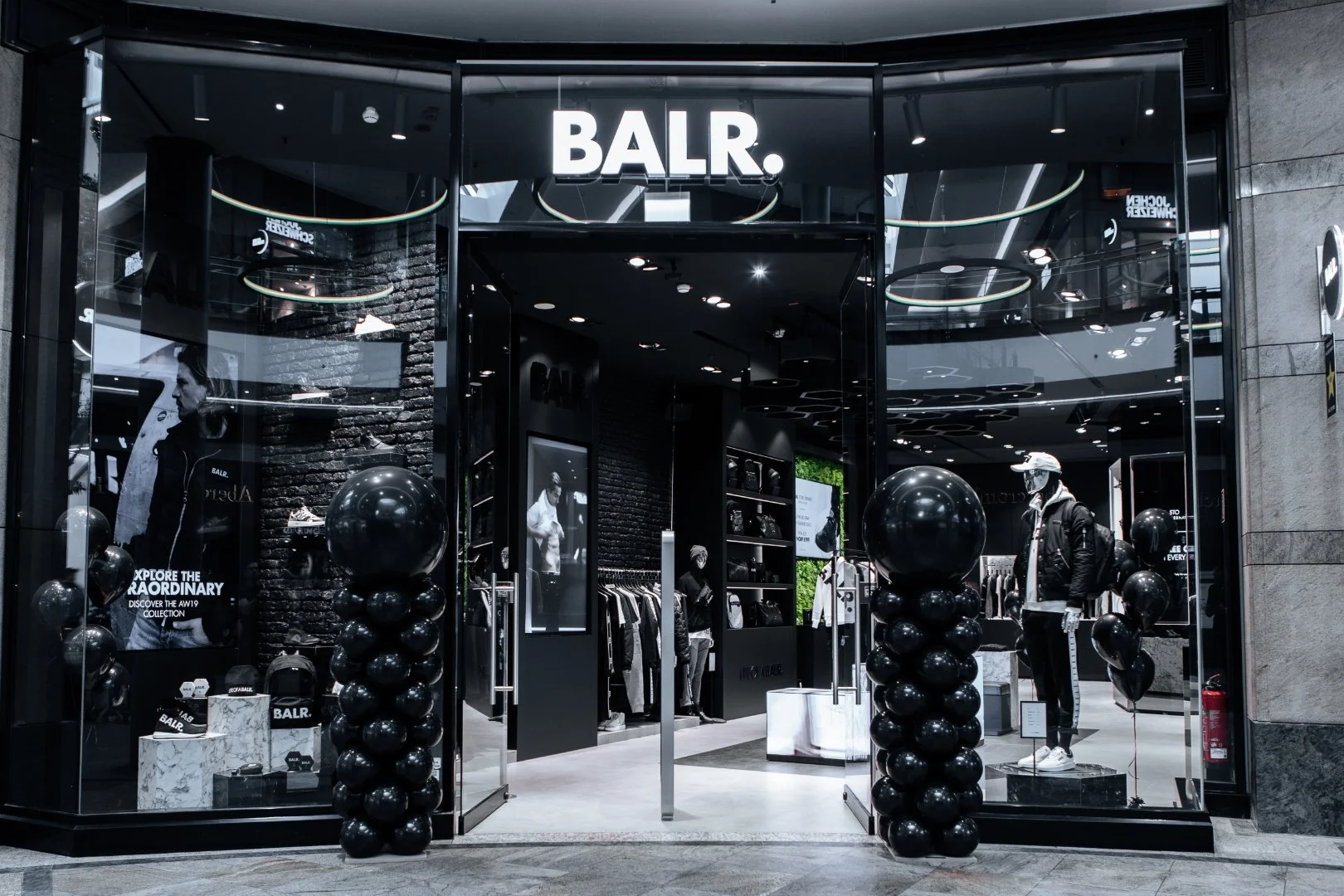 Storefront of BALR. clothing store with black balloons on either side of the entrance, mannequins dressed in casual sporty attire, and large black-and-white posters inside showcasing models and fashion items.