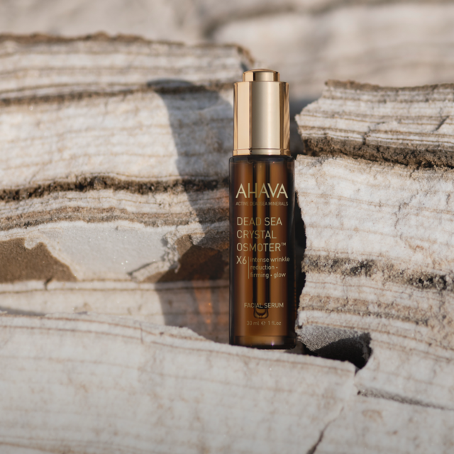 A bottle of AHAVA Dead Sea Crystal Osmoter facial serum placed on a piece of driftwood.