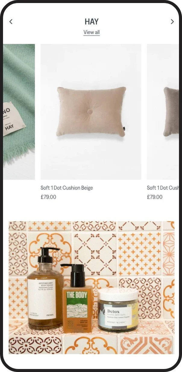 Collection of home decor and skincare products including a beige cushion pillow and various bottles of body wash, soap, and detox cream on patterned tiles.