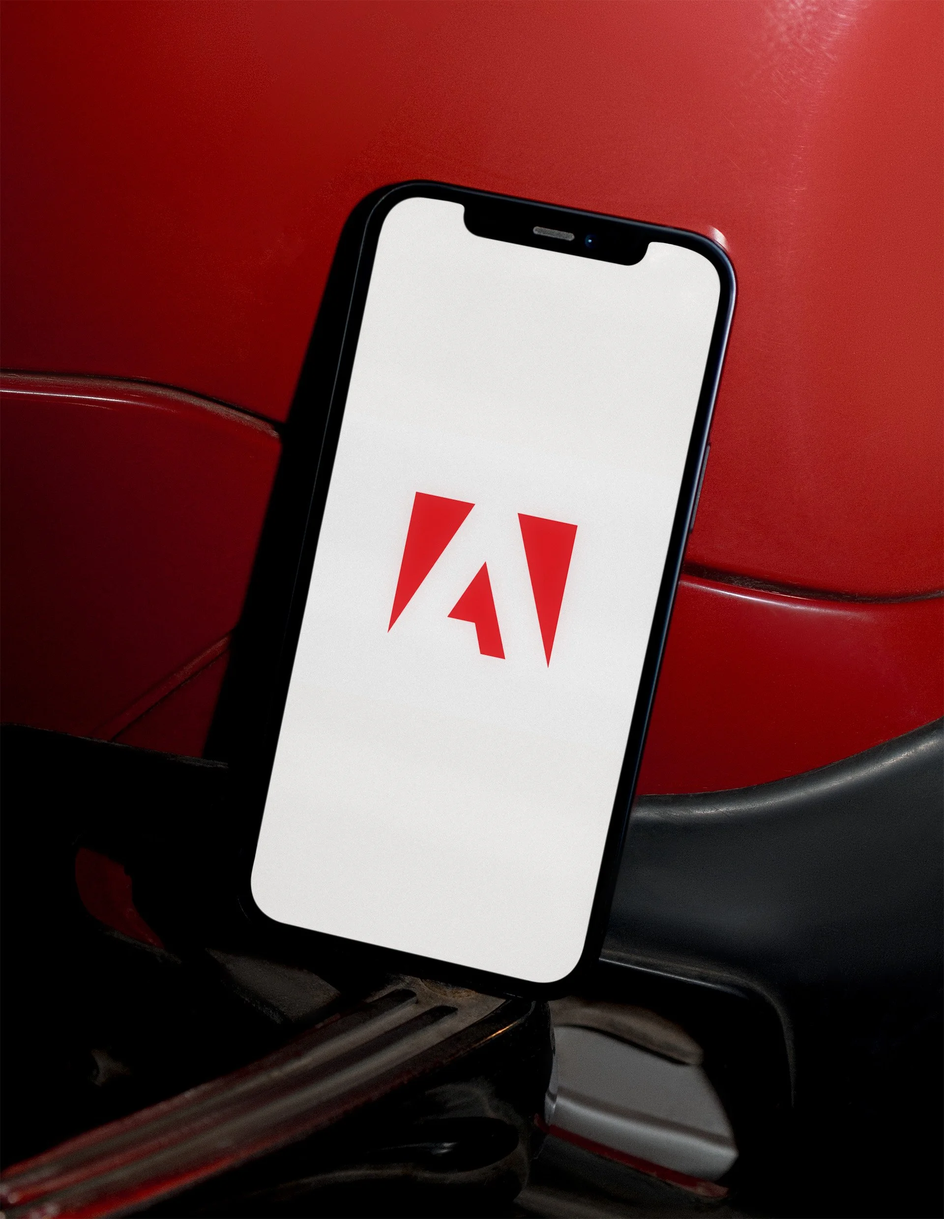 Smartphone displaying the Adobe logo resting against the seat of a red and black aircraft seat.