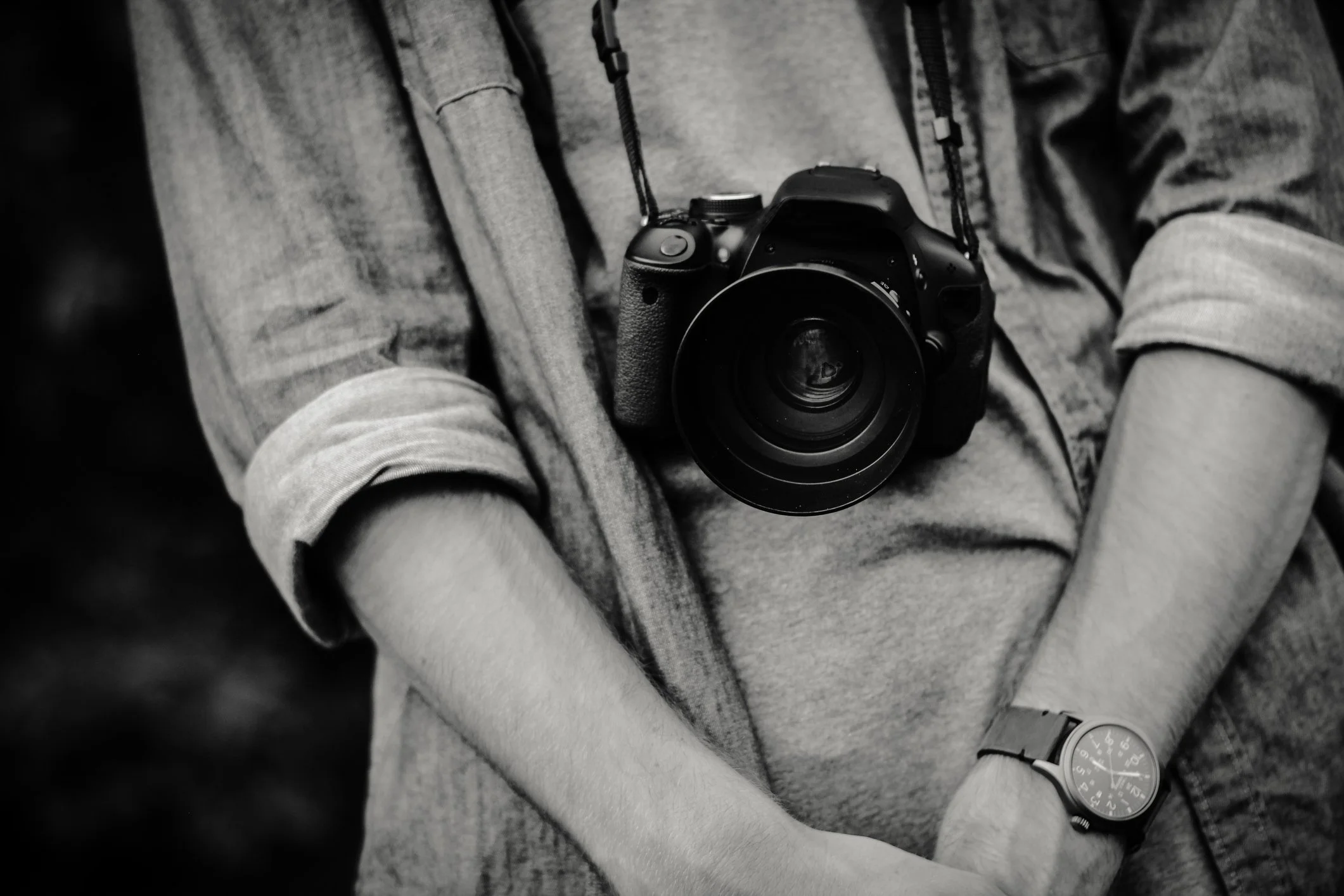 Person wearing a watch, with rolled up sleeves, holding a camera around neck
