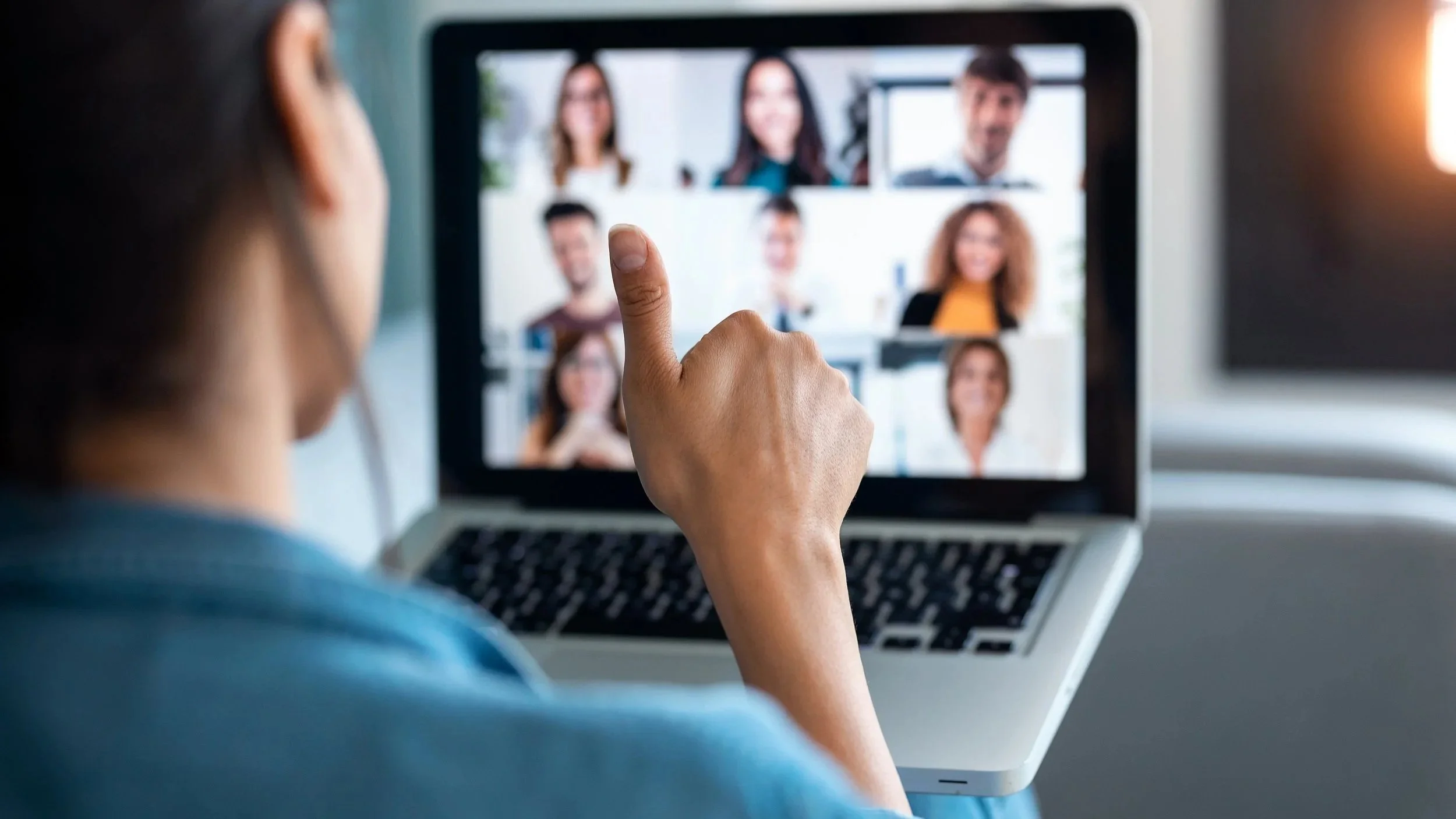 Person video conferencing with multiple people on a laptop screen, gesturing with a finger.