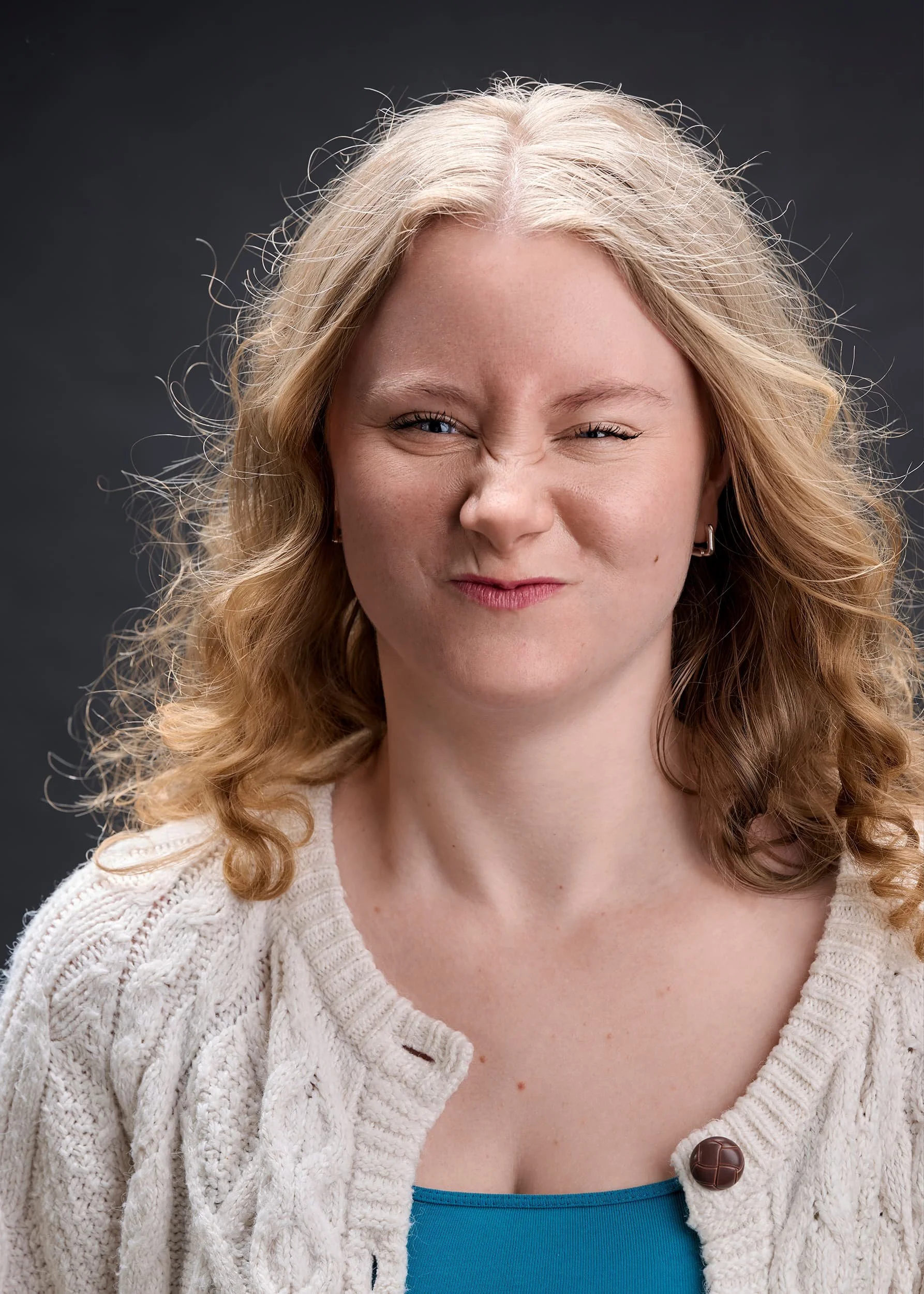 Professional actor headshot photograph of a woman with light blonde, curly hair making a scrunched face and wincing.