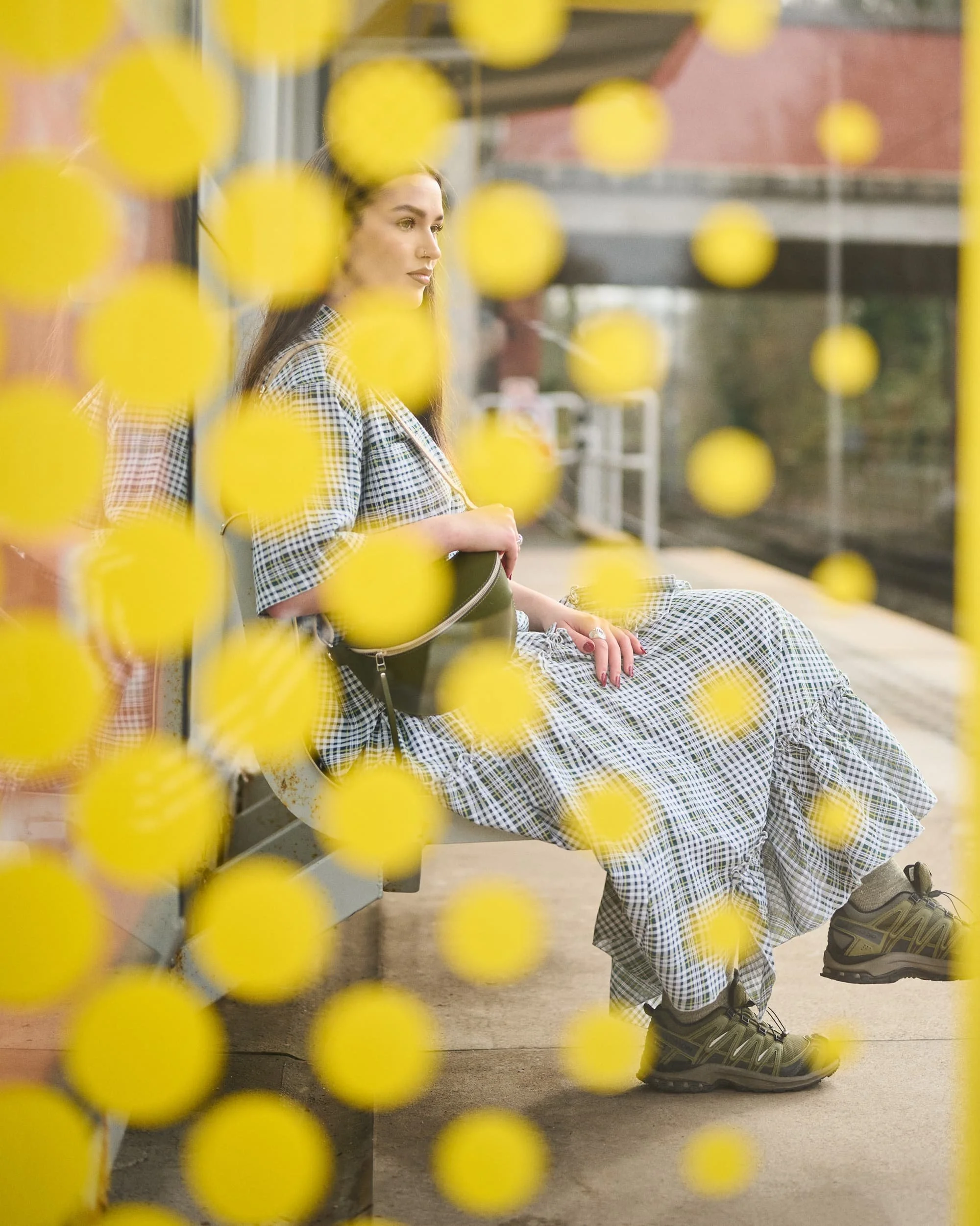A woman sitting on a bench at a train station platform, seen through a yellow dotted barrier.