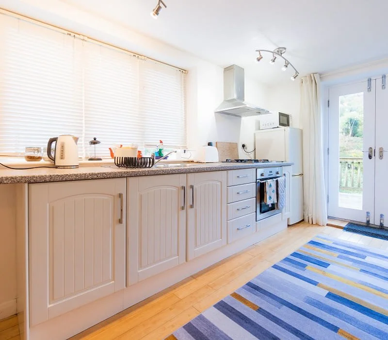 Bright kitchen with white cabinets, countertop appliances, and a view of a deck through glass doors.